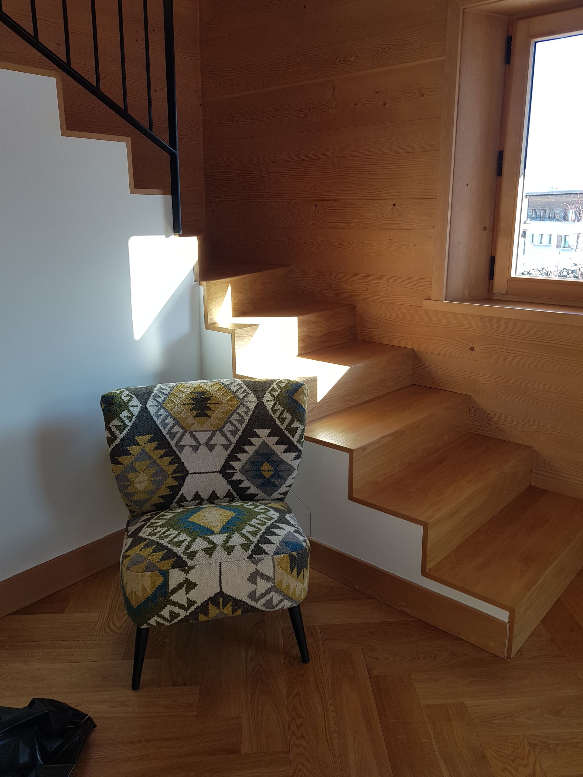Un fauteuil recouvert de tissu à motifs est placé à côté d'un escalier en bois. La lumière du soleil illumine les marches.
