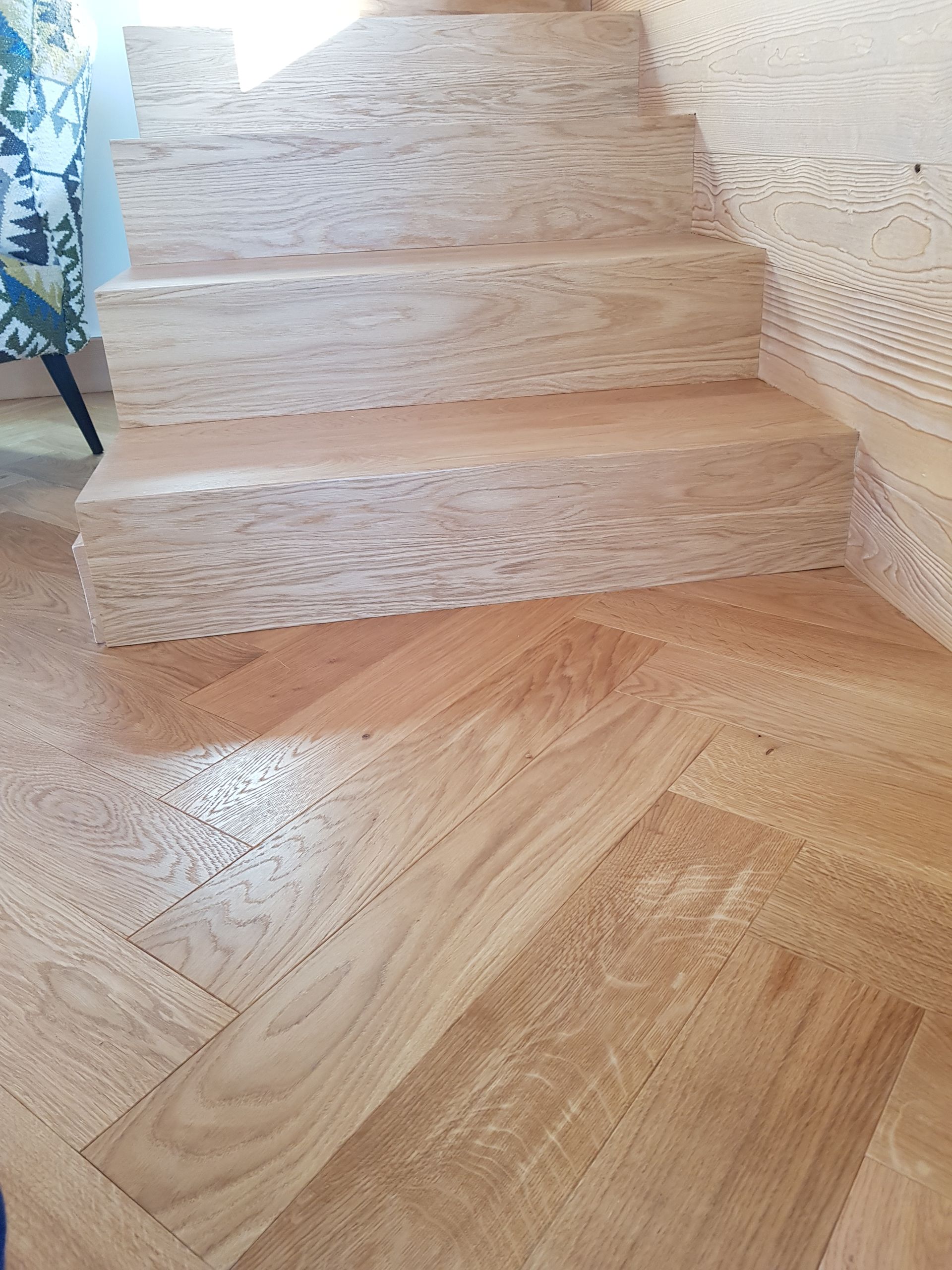 Escalier en bois et parquet à chevrons, lumière naturelle, menant à l'étage.