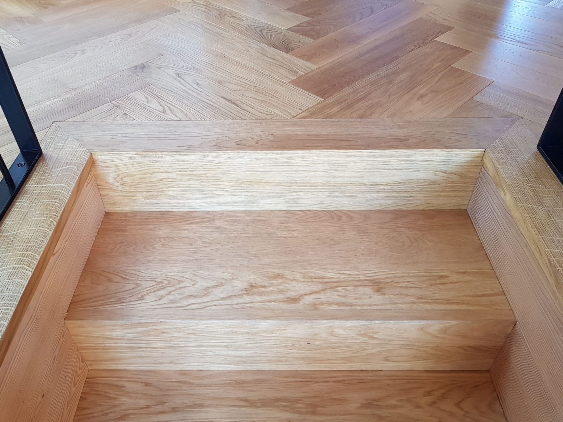 Un escalier en bois descend, entouré d'un parquet clair.