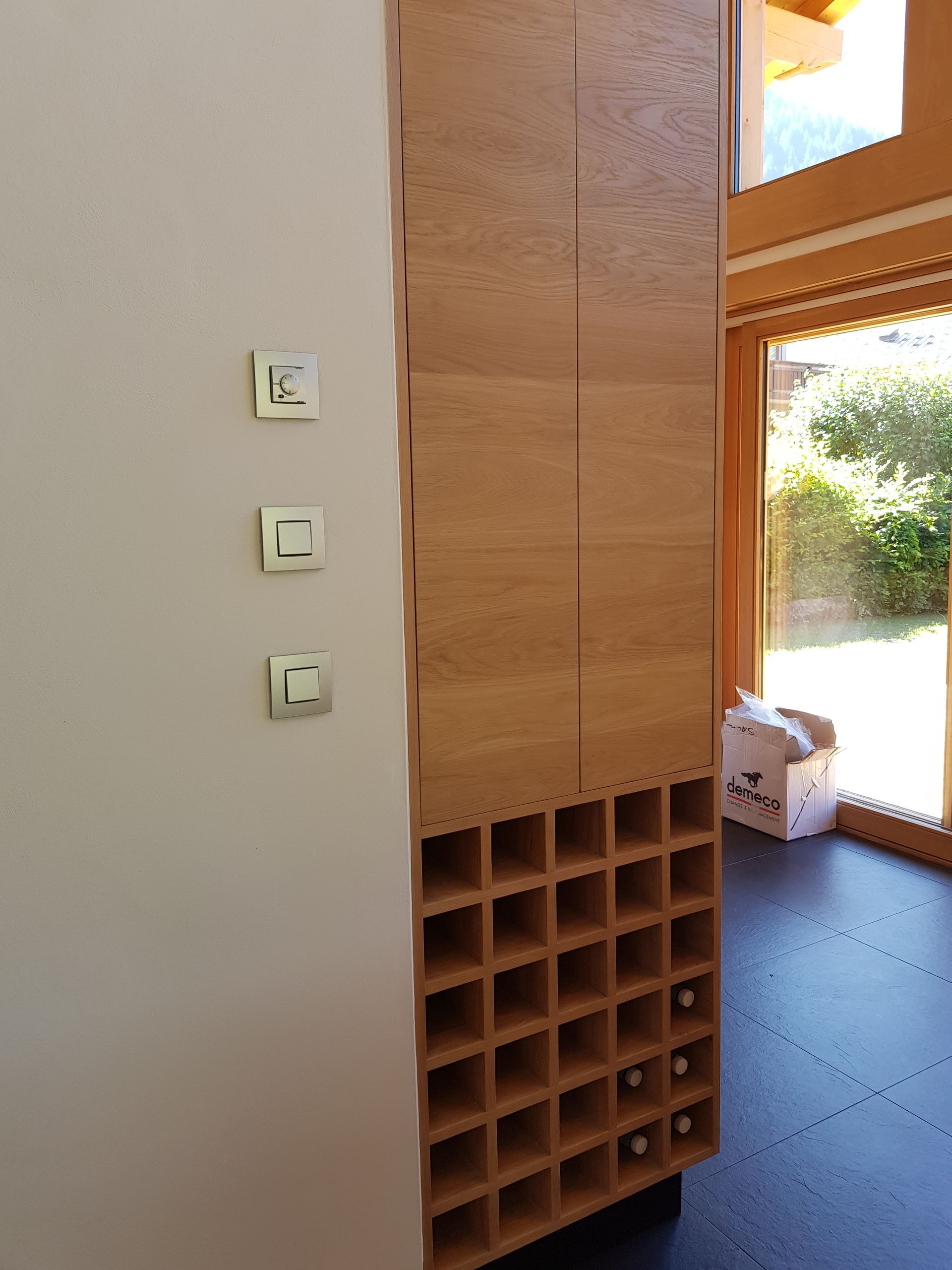 Casier à vin en bois intégré au mur, avec bouteilles et interrupteurs fixés au mur.