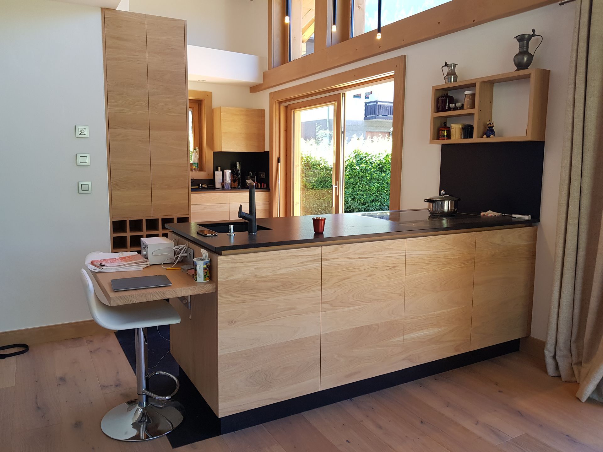 Cuisine moderne avec armoires en chêne, comptoirs noirs et îlot central avec sièges.