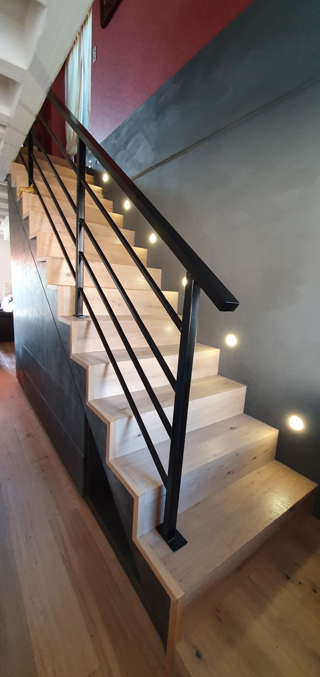 Escalier avec marches claires, rampe noire et éclairage intégré le long des marches et du mur.