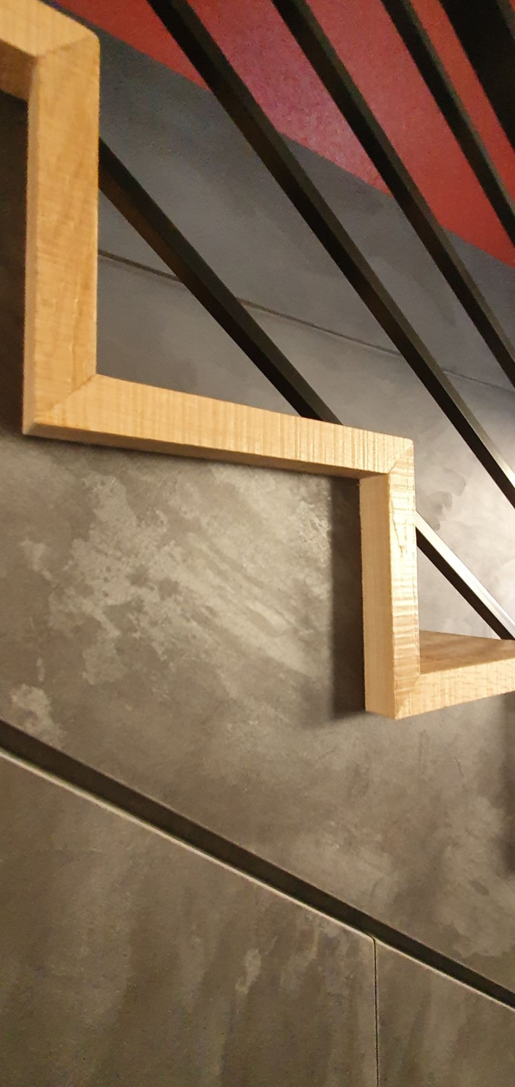 Cadres en bois en zigzag sur un mur gris moucheté, avec des rayures rouges et noires en arrière-plan.