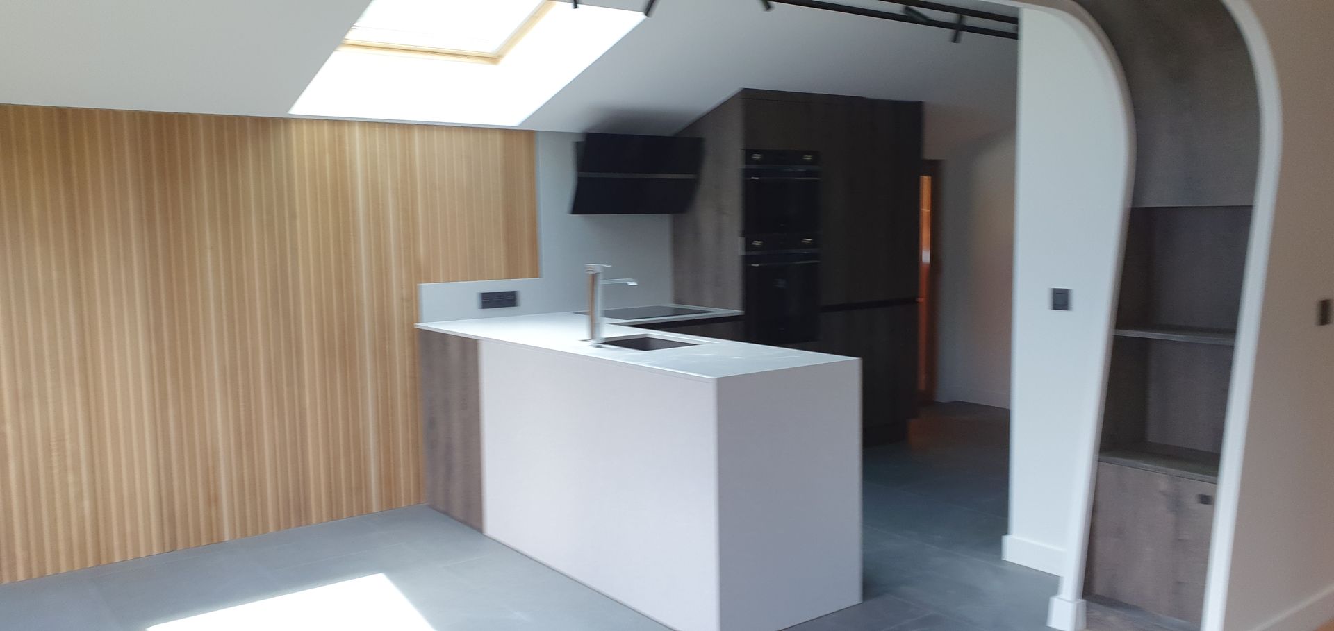 Cuisine moderne avec mur lambrissé, îlot blanc et appareils électroménagers intégrés.