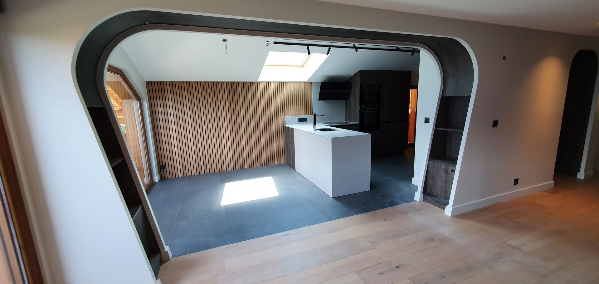 Intérieur d'une maison moderne avec des portes cintrées, une cuisine et un mur d'accent en bois.