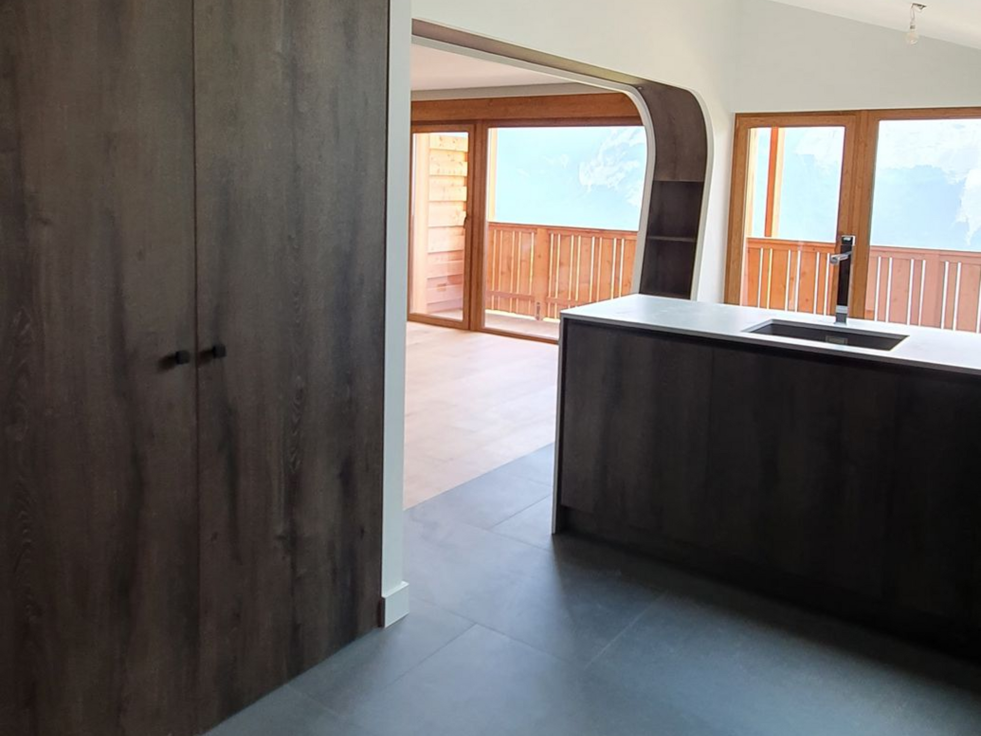 Couloir intérieur avec meubles en bois foncé, sol foncé et éclairage sur rail.