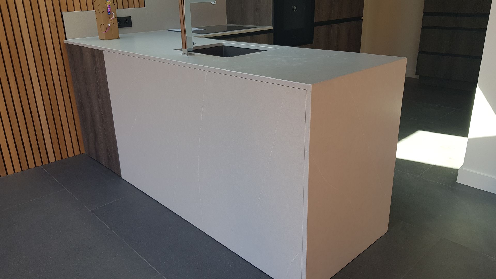 Îlot de cuisine blanc avec plan de travail et évier gris, à côté de lambris.