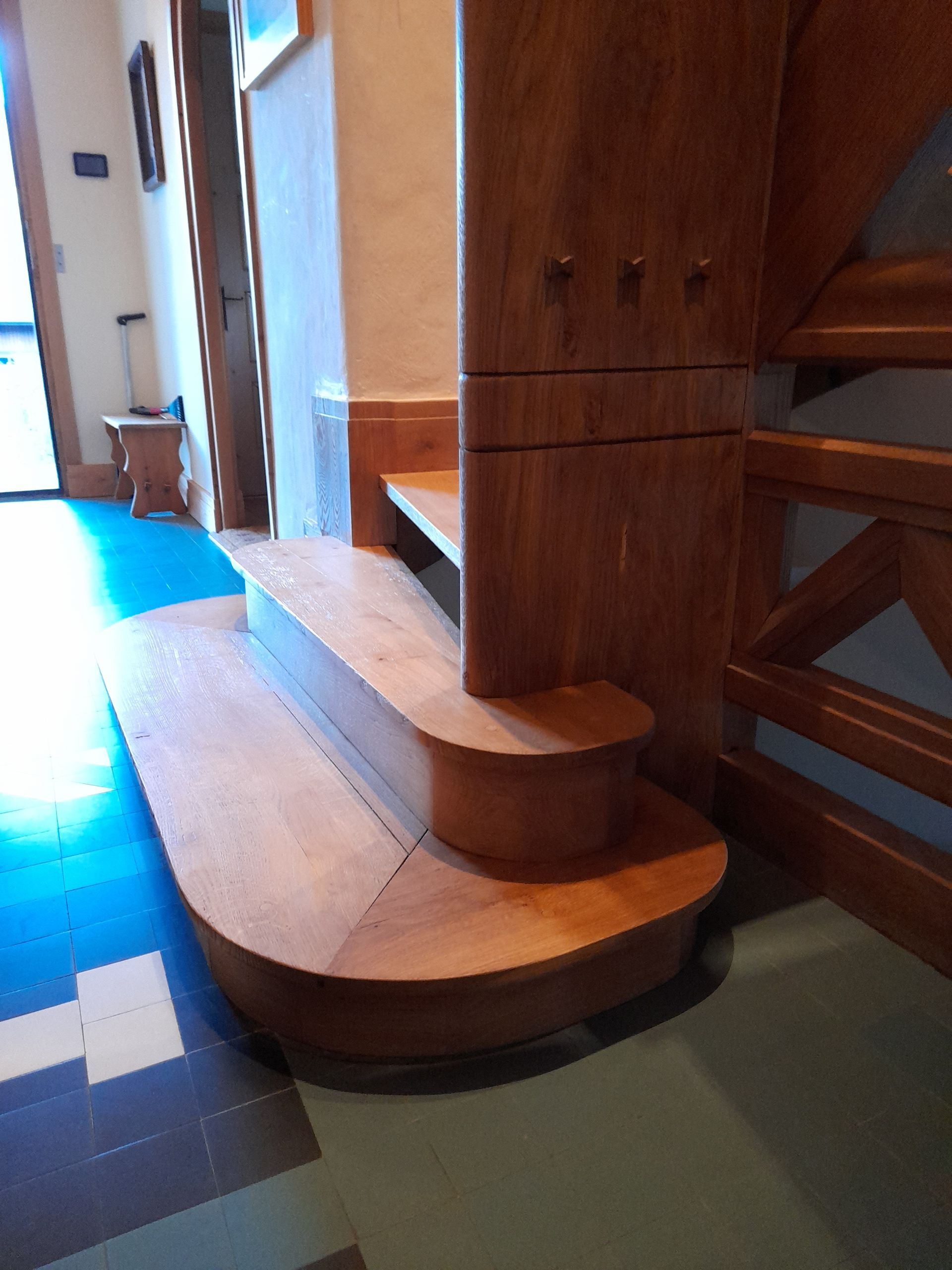 Escalier en bois à marches courbes, fixé à un poteau par des crochets, dans un couloir.