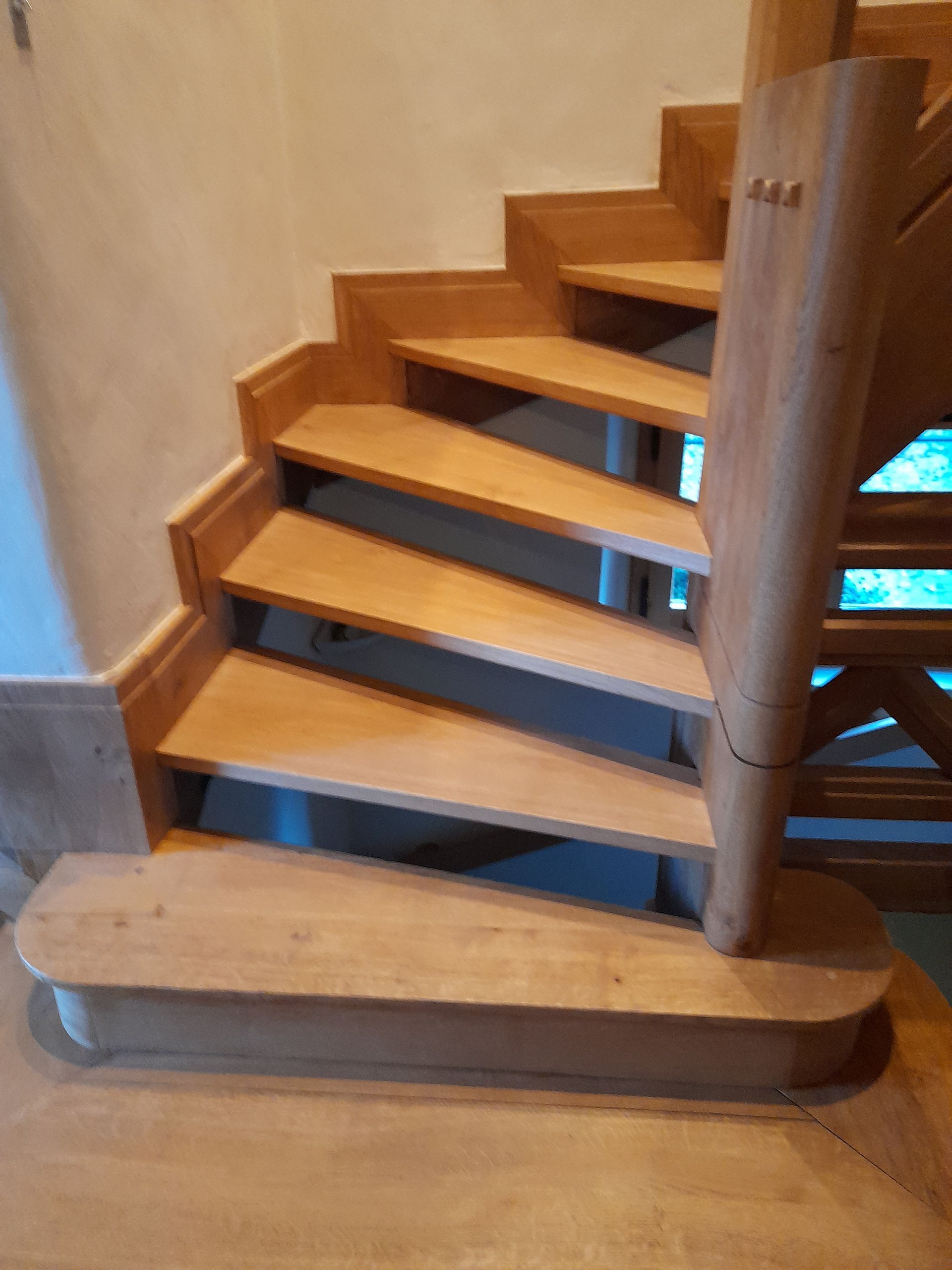 Escalier en colimaçon en bois avec marches brun clair et poteau de départ arrondi.