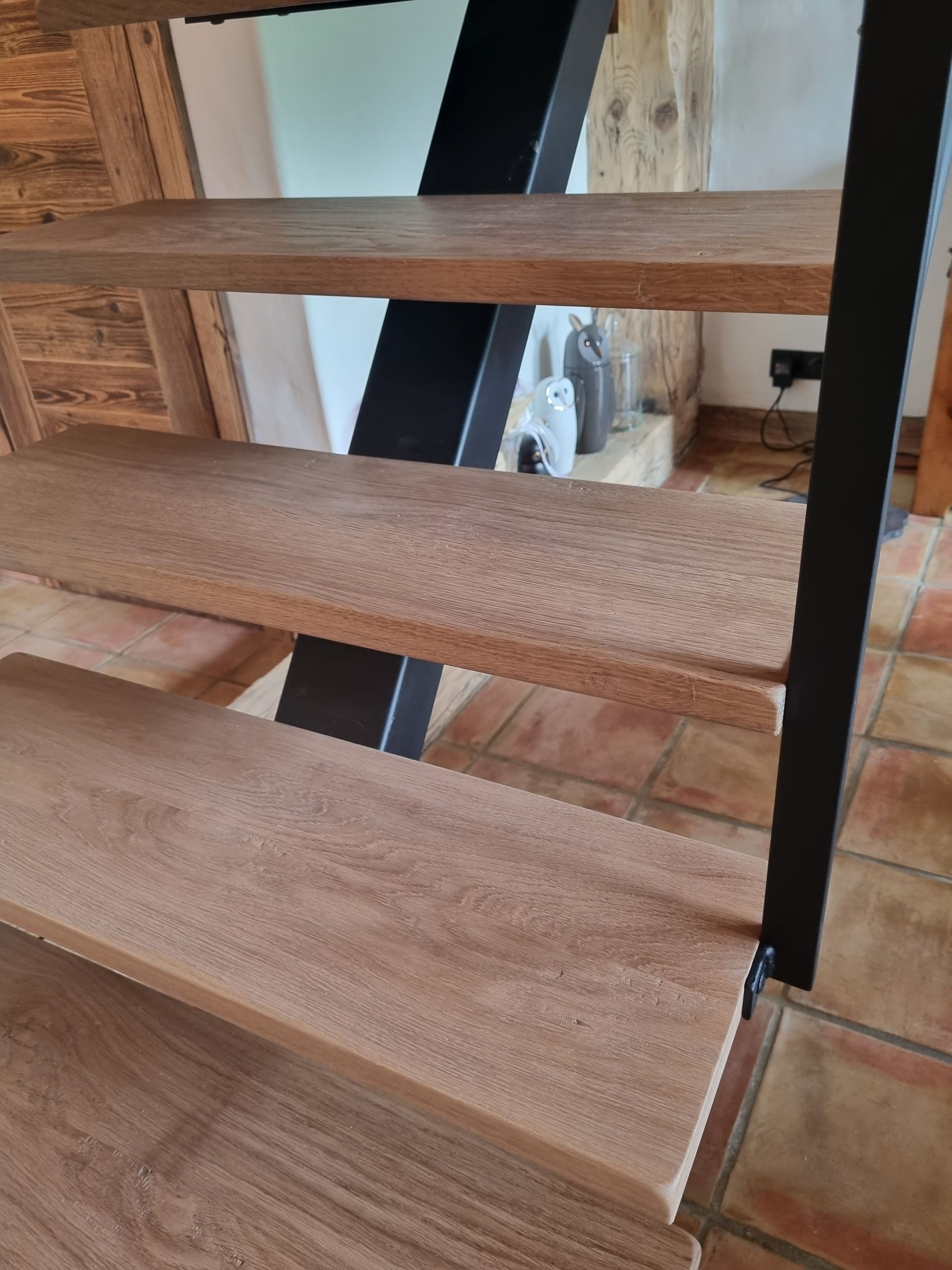 Marches d'escalier en bois avec support en métal noir sur fond de mur clair.