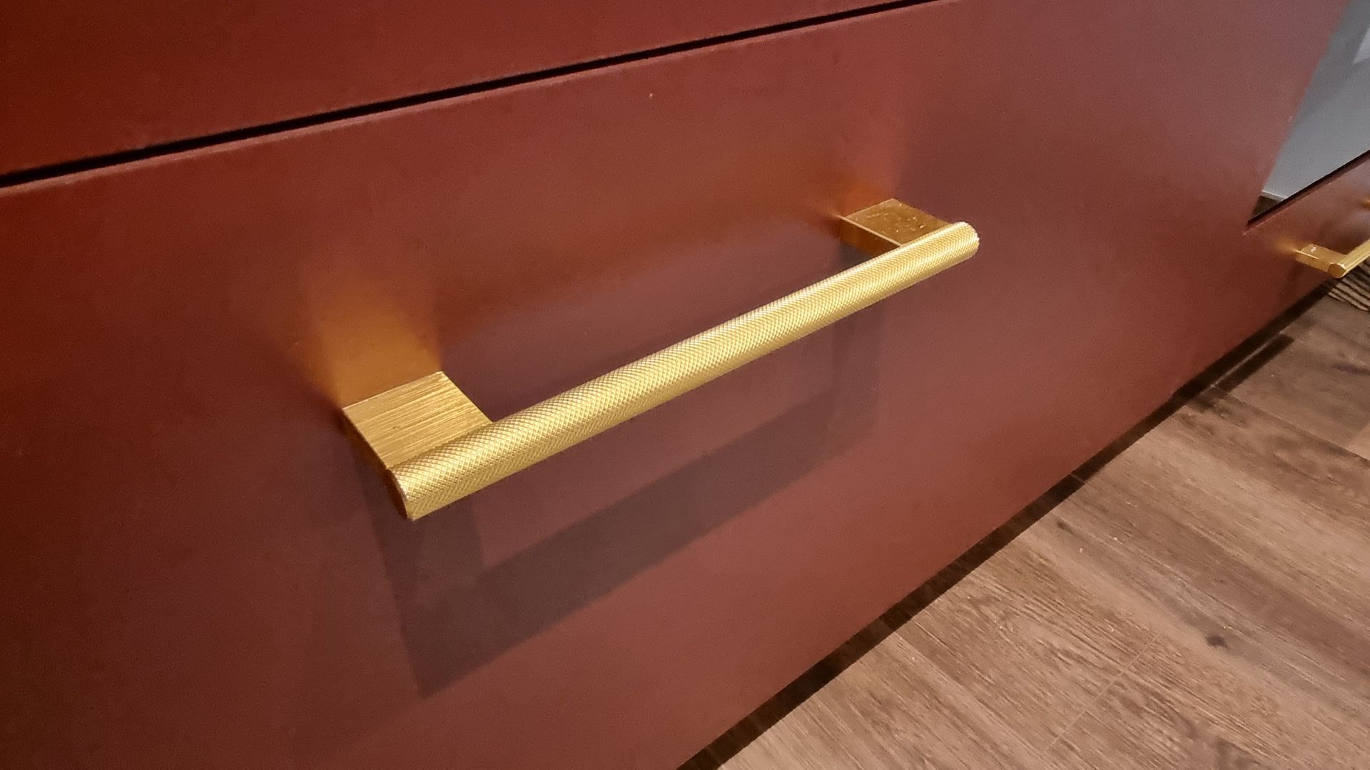 Poignée texturée dorée sur une porte d'armoire rouge foncé ; vue rapprochée.