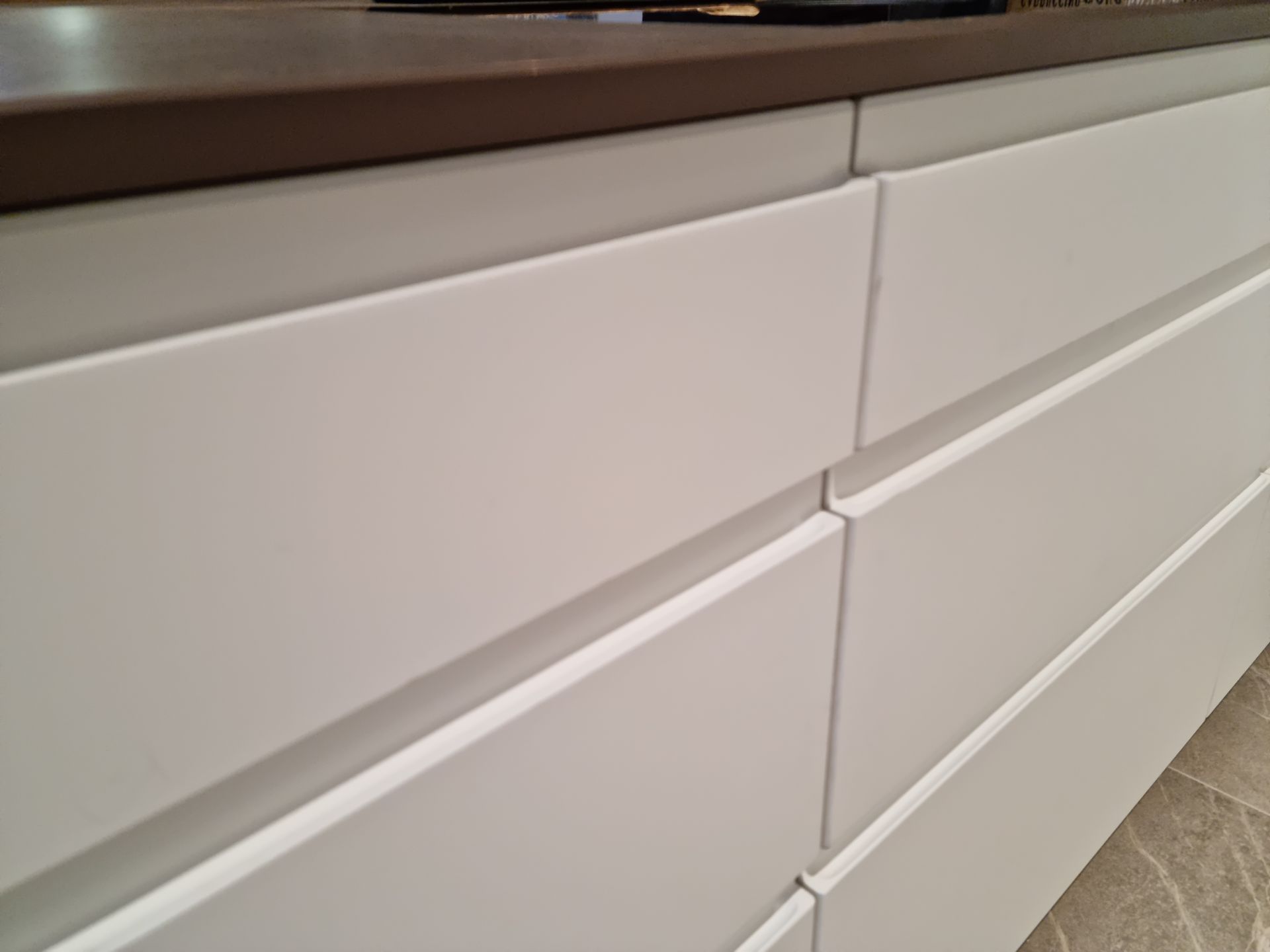 Tiroirs de placards de cuisine blancs avec poignées horizontales encastrées, sous un plan de travail foncé.