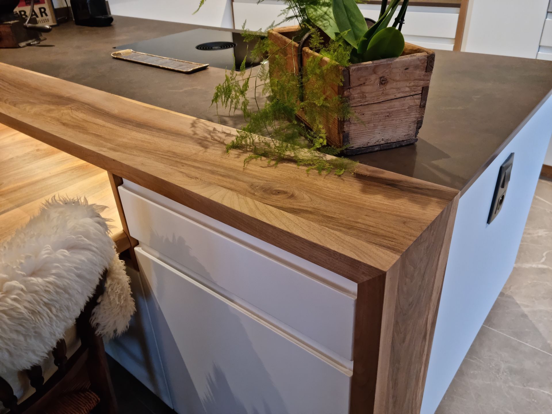 Îlot de cuisine avec un plan de travail en bois et des placards blancs, agrémenté d'une plante en pot.