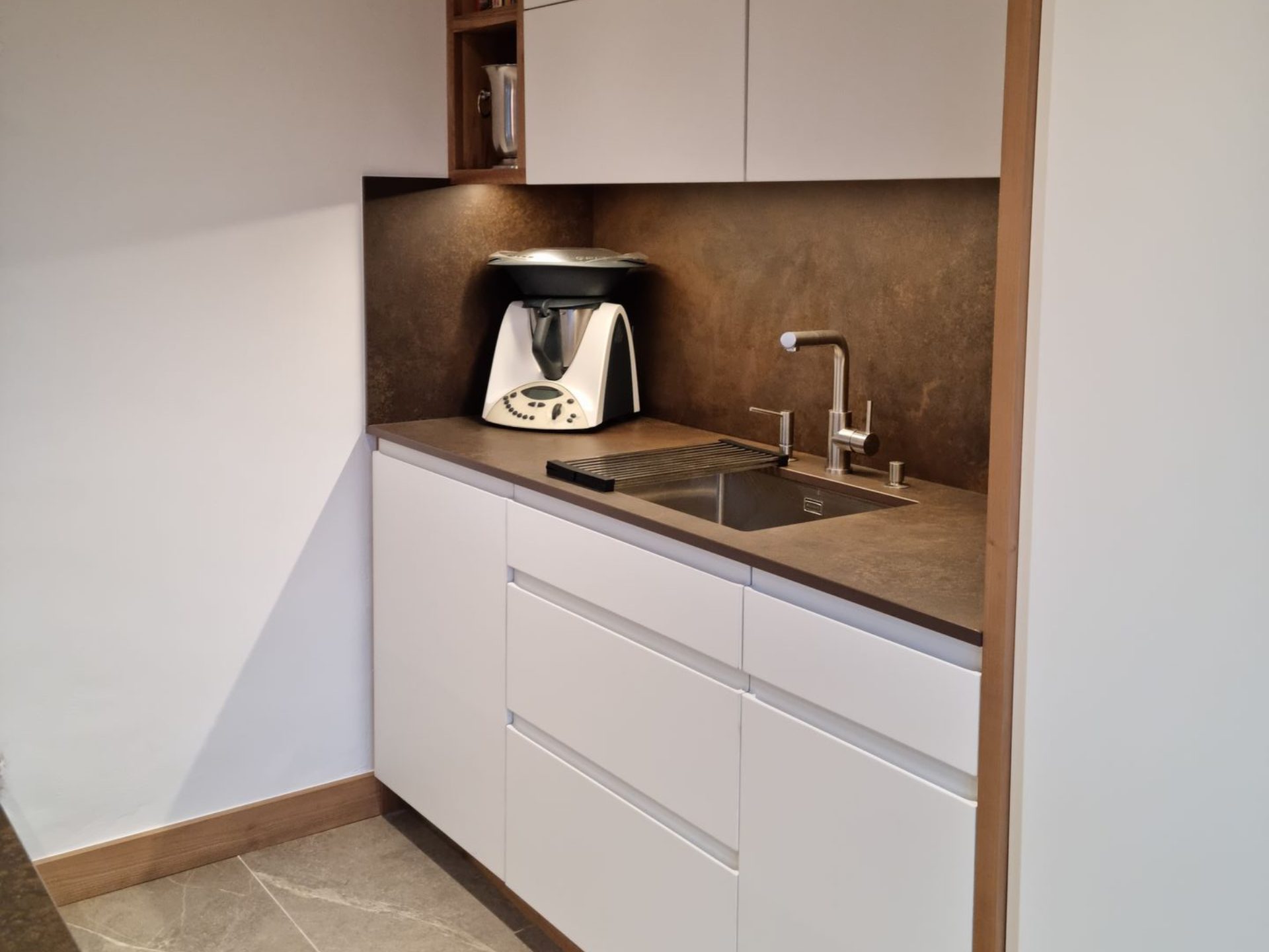 Coin cuisine moderne avec évier, tiroirs et appareil électroménager sur le plan de travail.