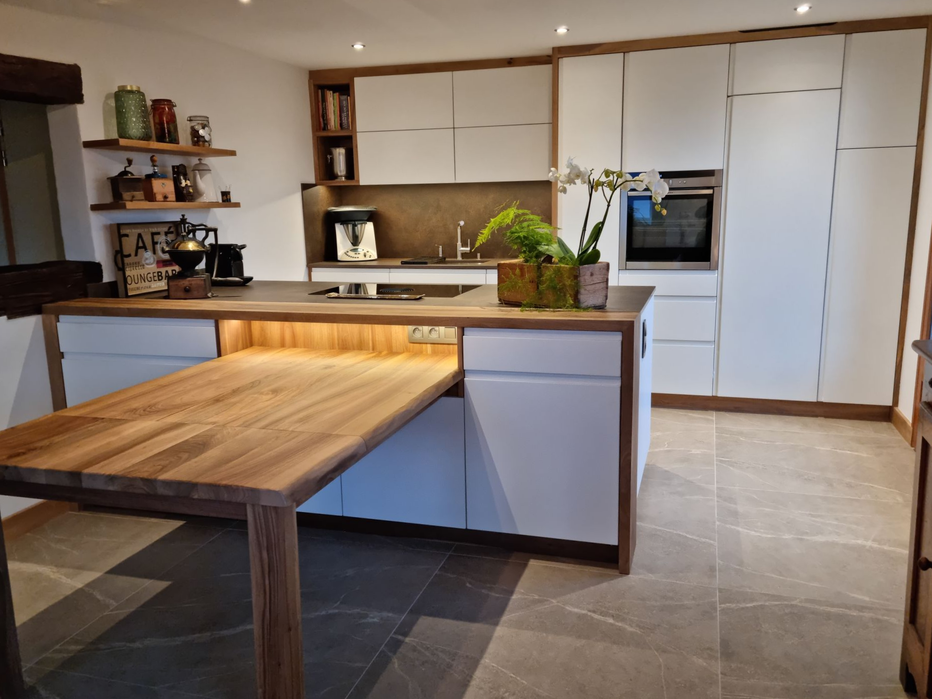 Cuisine moderne avec placards blancs, finitions en bois et table coulissante en bois.