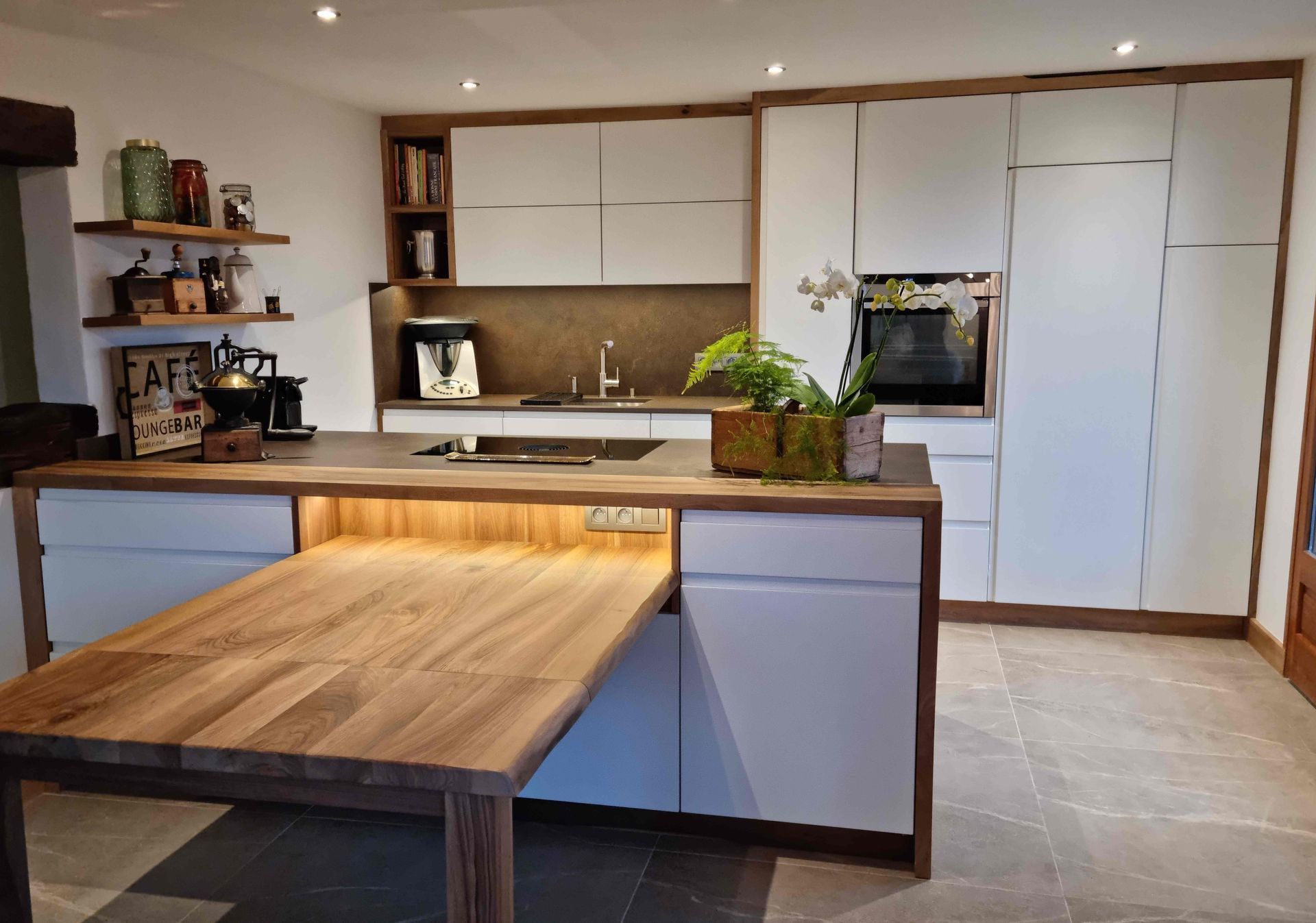 Cuisine moderne avec placards blancs, touches de bois et table coulissante.