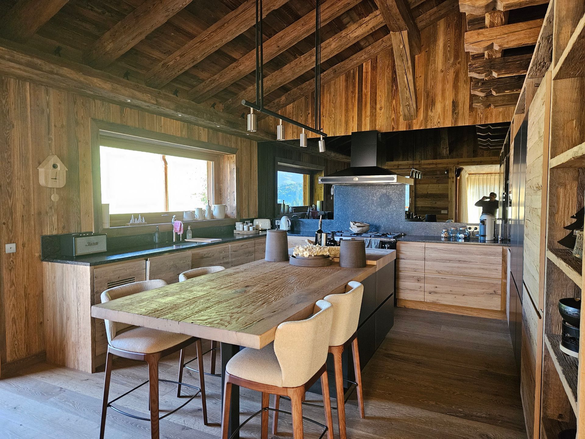 Cuisine rustique avec murs en bois, îlot et longue table en bois avec chaises.