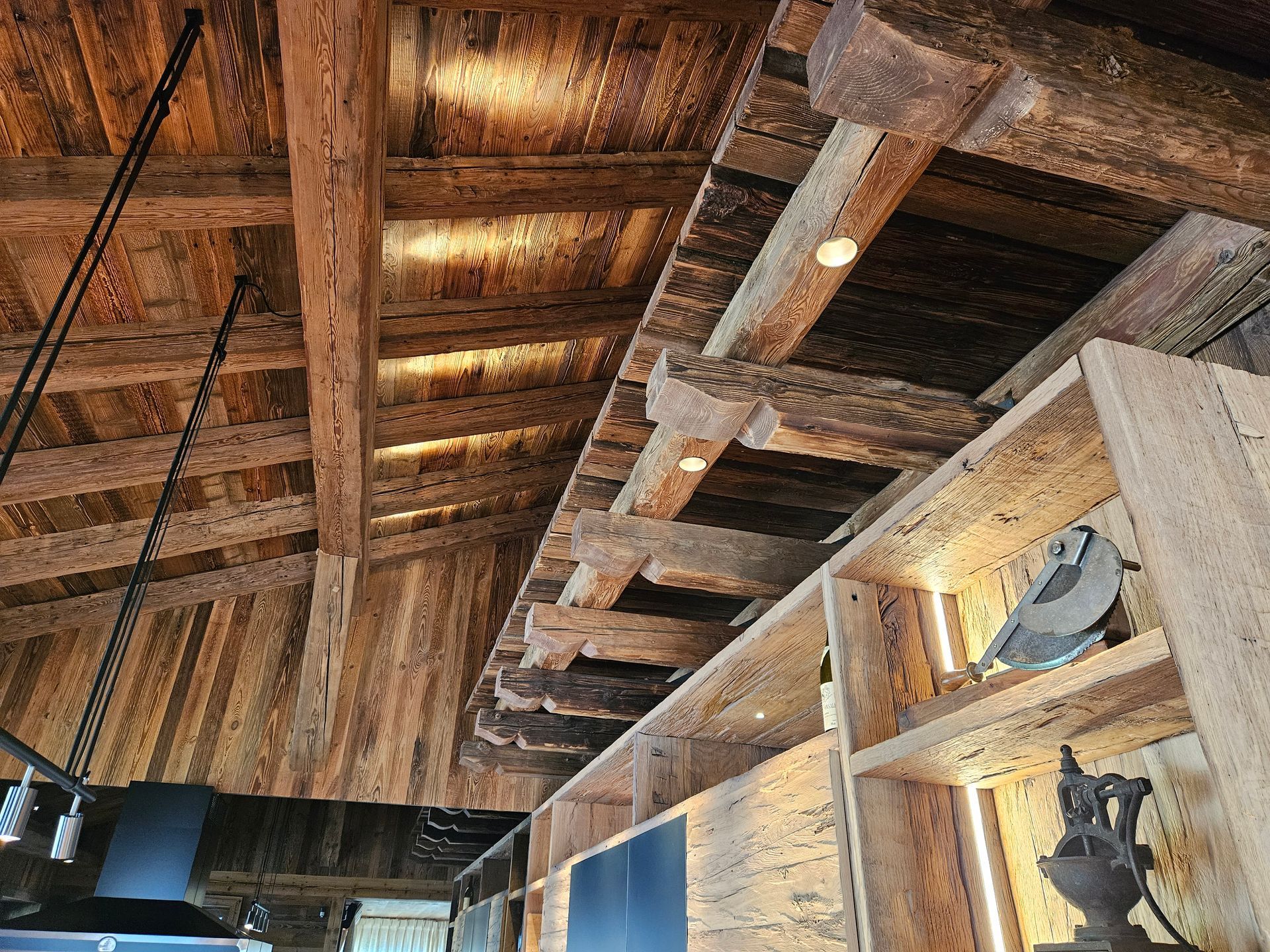 Plafond en bois avec poutres apparentes, luminaires encastrés et étagères intégrées avec objets décoratifs.