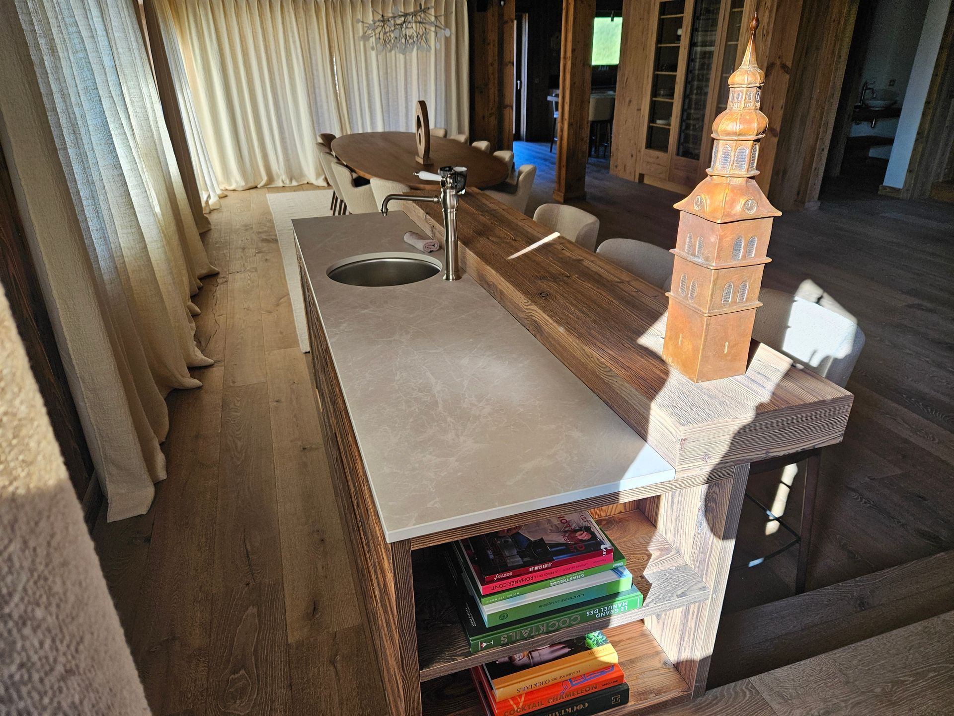 Îlot de cuisine avec comptoir en béton, étagères en bois et sculpture de tour décorative.