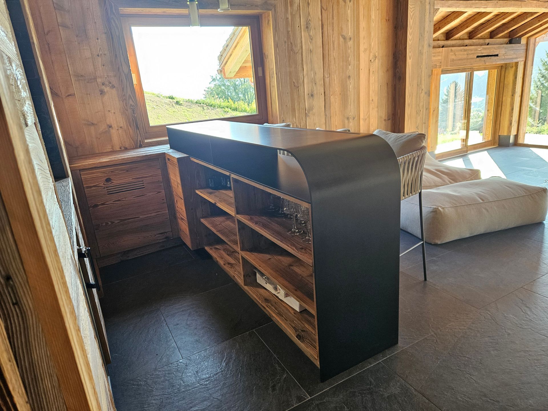 Armoire en bois et noire avec étagères ouvertes dans une pièce avec boiseries et sol en pierre.