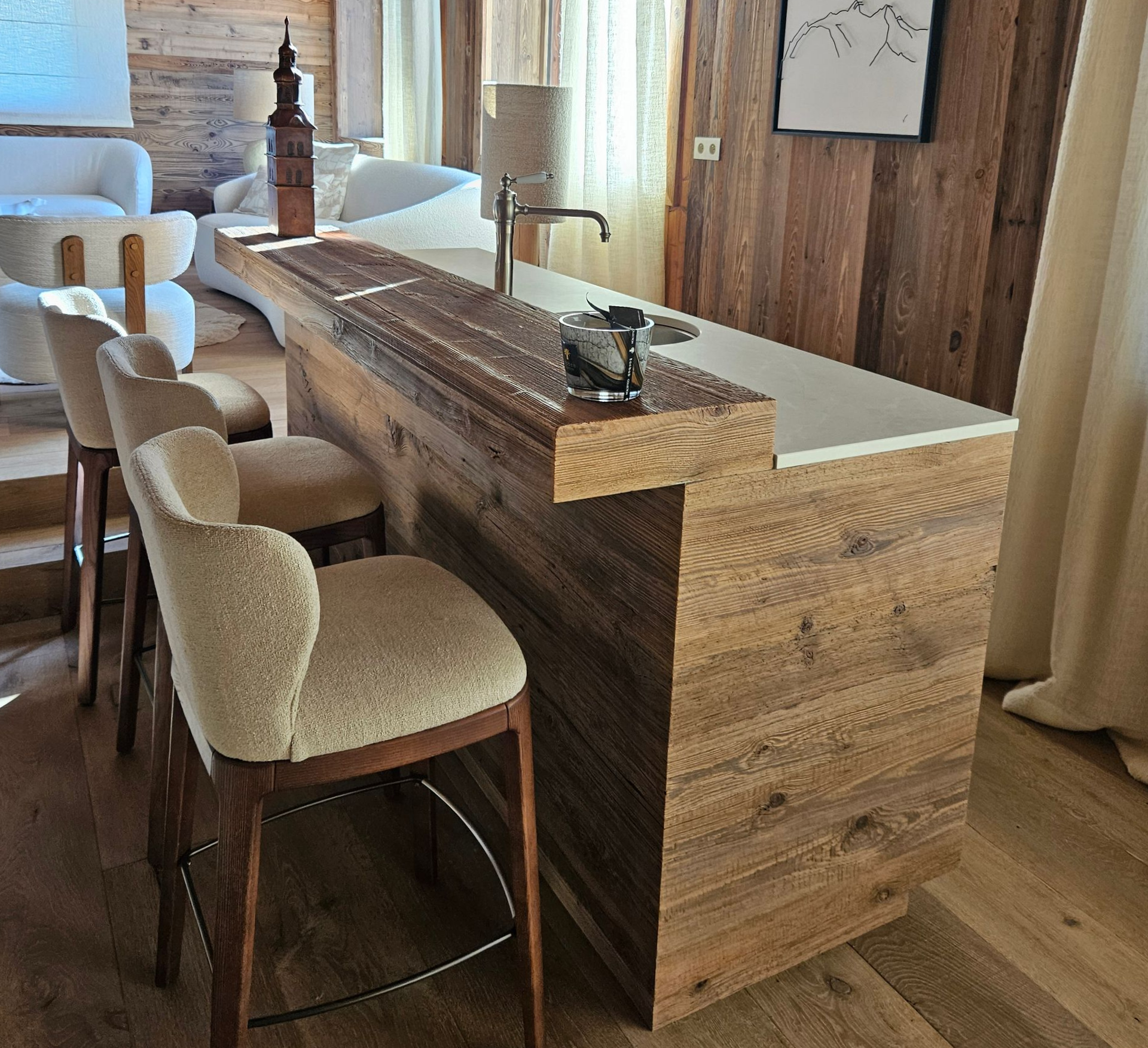 Bar en bois avec comptoir blanc, trois tabourets de bar et un petit évier.