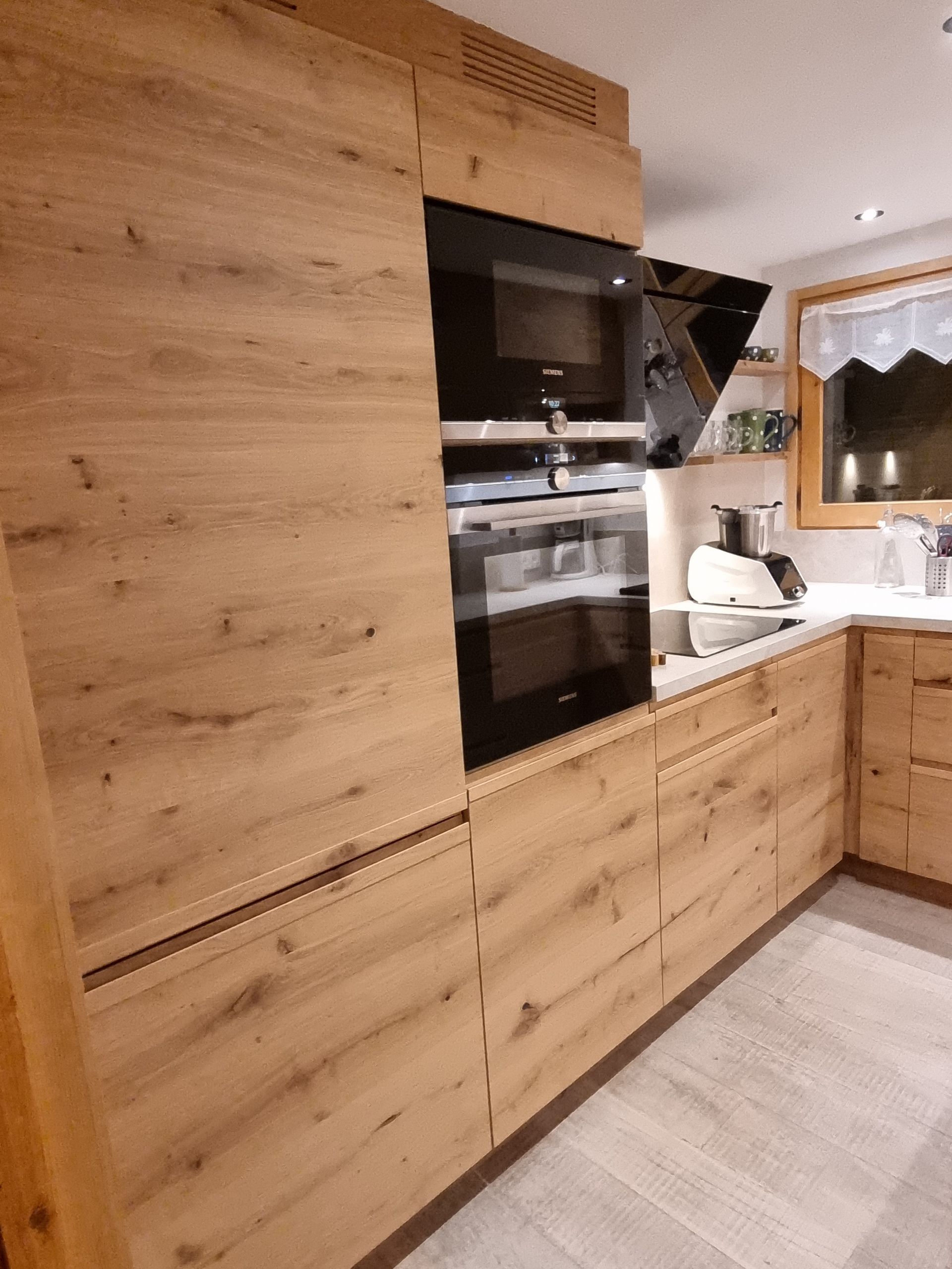 Cuisine équipée d'éléments en bois, d'un four intégré et d'une hotte aspirante ; une fenêtre est visible en arrière-plan.