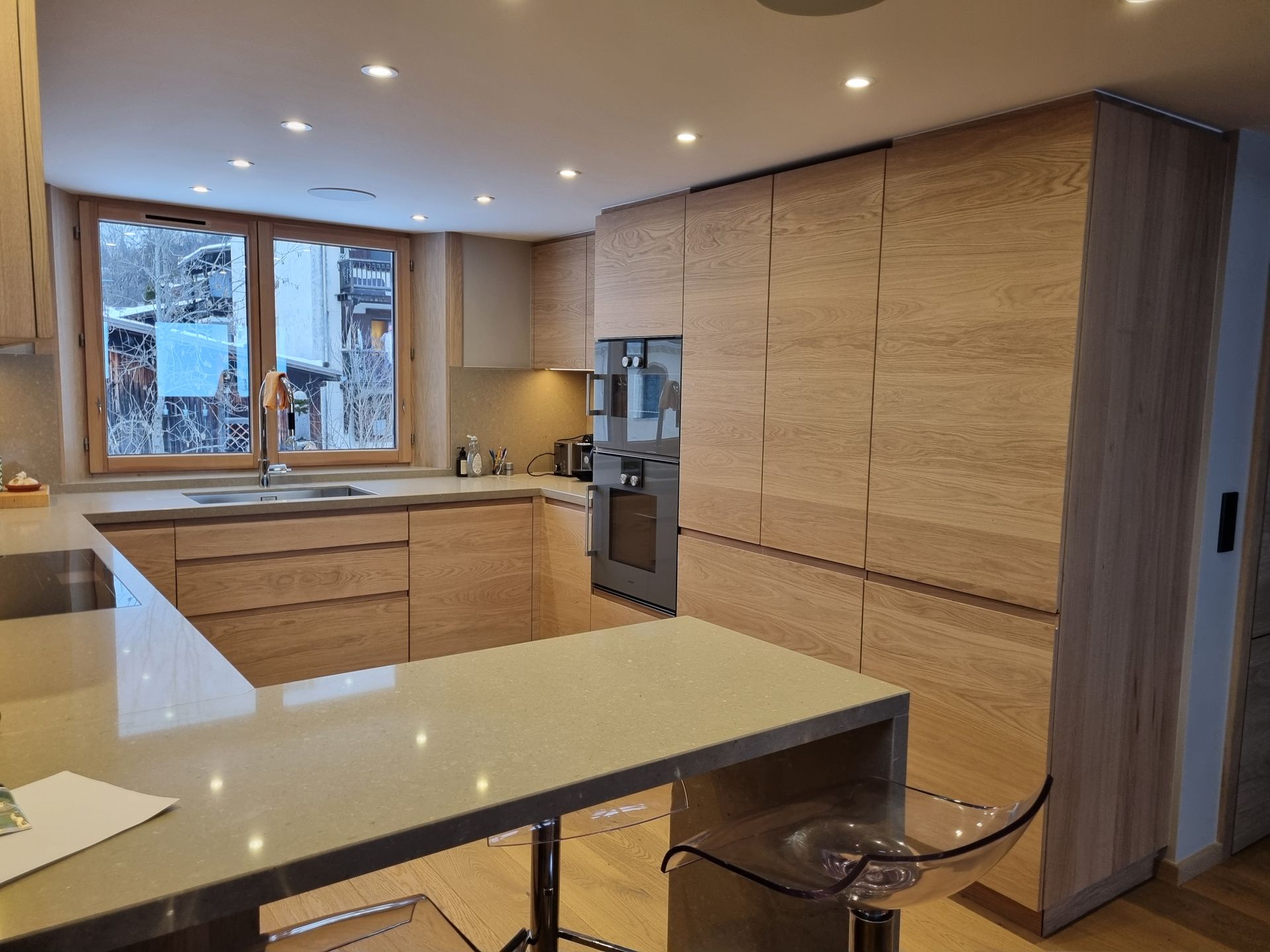 Cuisine moderne avec placards en bois clair, four encastré et bar pour le petit-déjeuner.