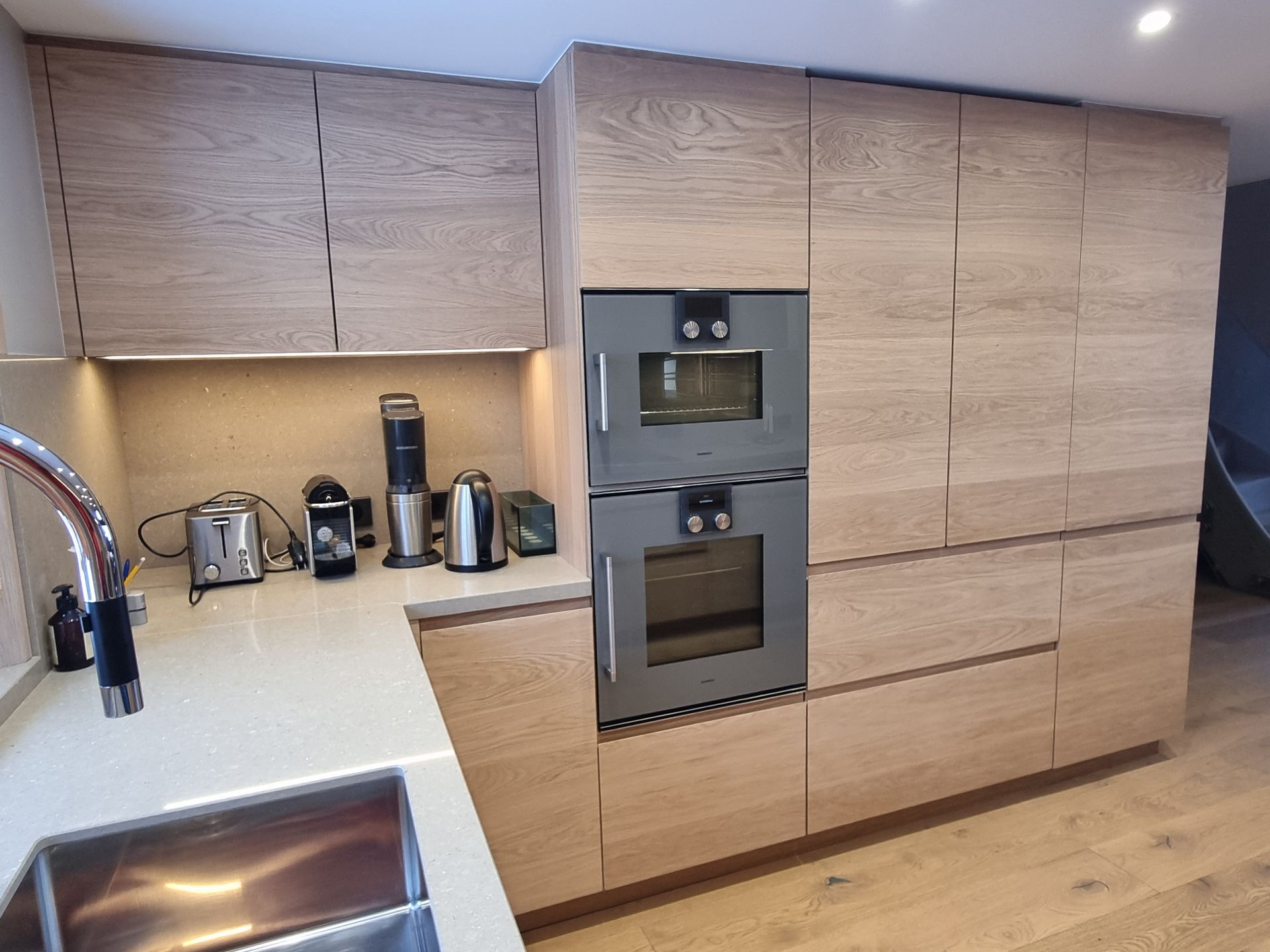 Cuisine moderne avec placards en bois clair, fours encastrés et appareils électroménagers sur le plan de travail.