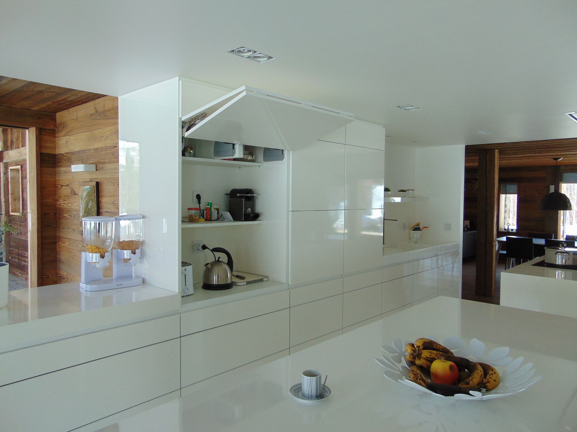 Cuisine blanche moderne avec placards intégrés et étagère ouverte. Le plan de travail est agrémenté d'une corbeille de fruits et d'une tasse à thé.