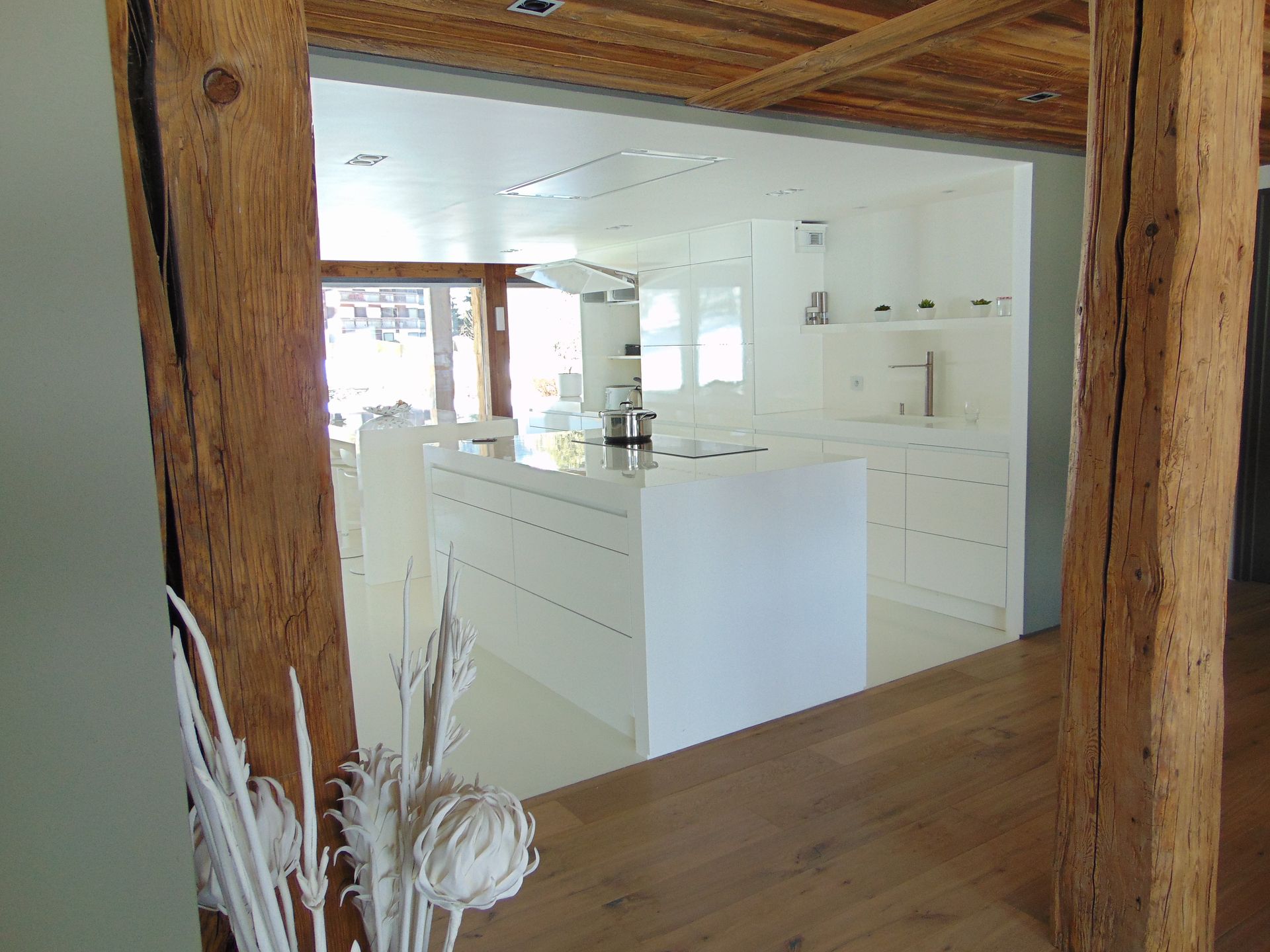 Des poutres en bois encadrent une cuisine moderne, lumineuse et blanche.