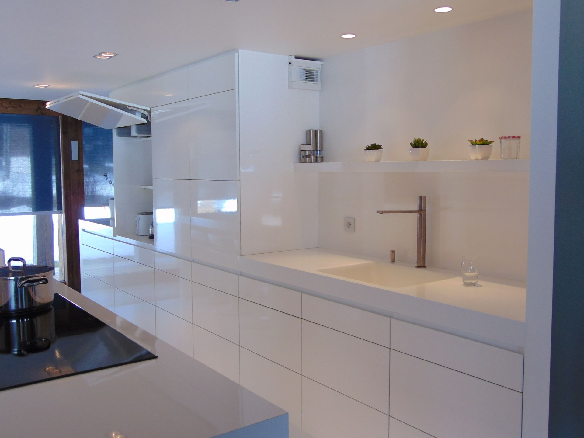 Cuisine moderne blanche avec des armoires élégantes, un évier intégré et un robinet en acier inoxydable ; plantes en pot sur une étagère.