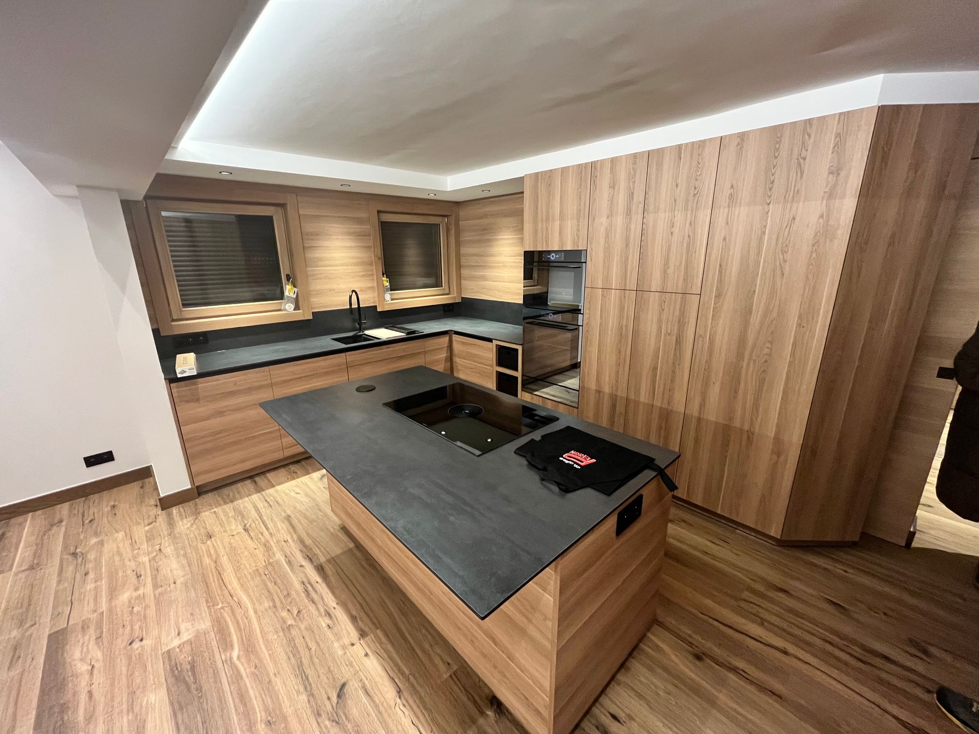 Cuisine moderne avec placards en bois, îlot central et plan de travail foncé.