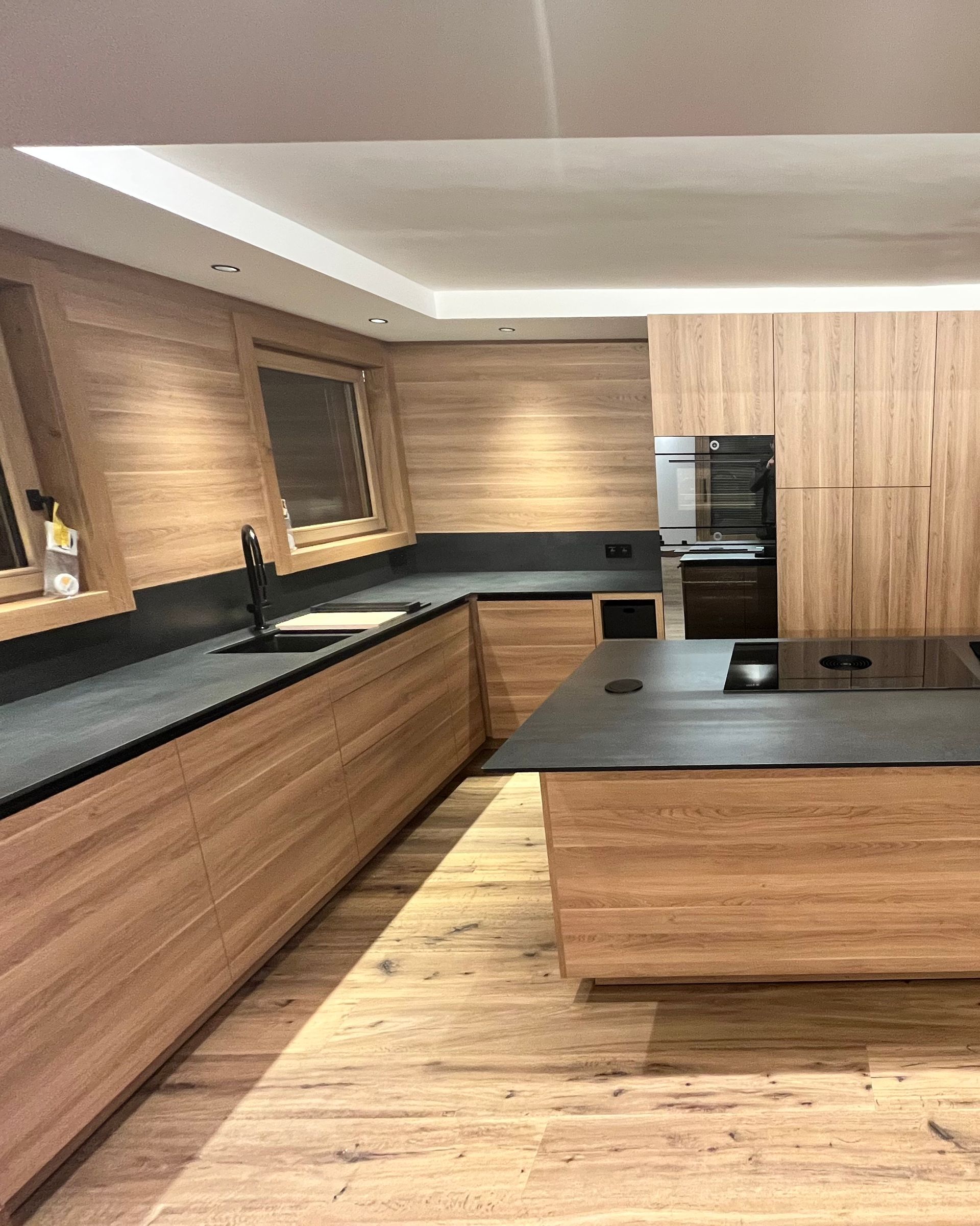 Cuisine en bois avec plans de travail noirs et îlot central.