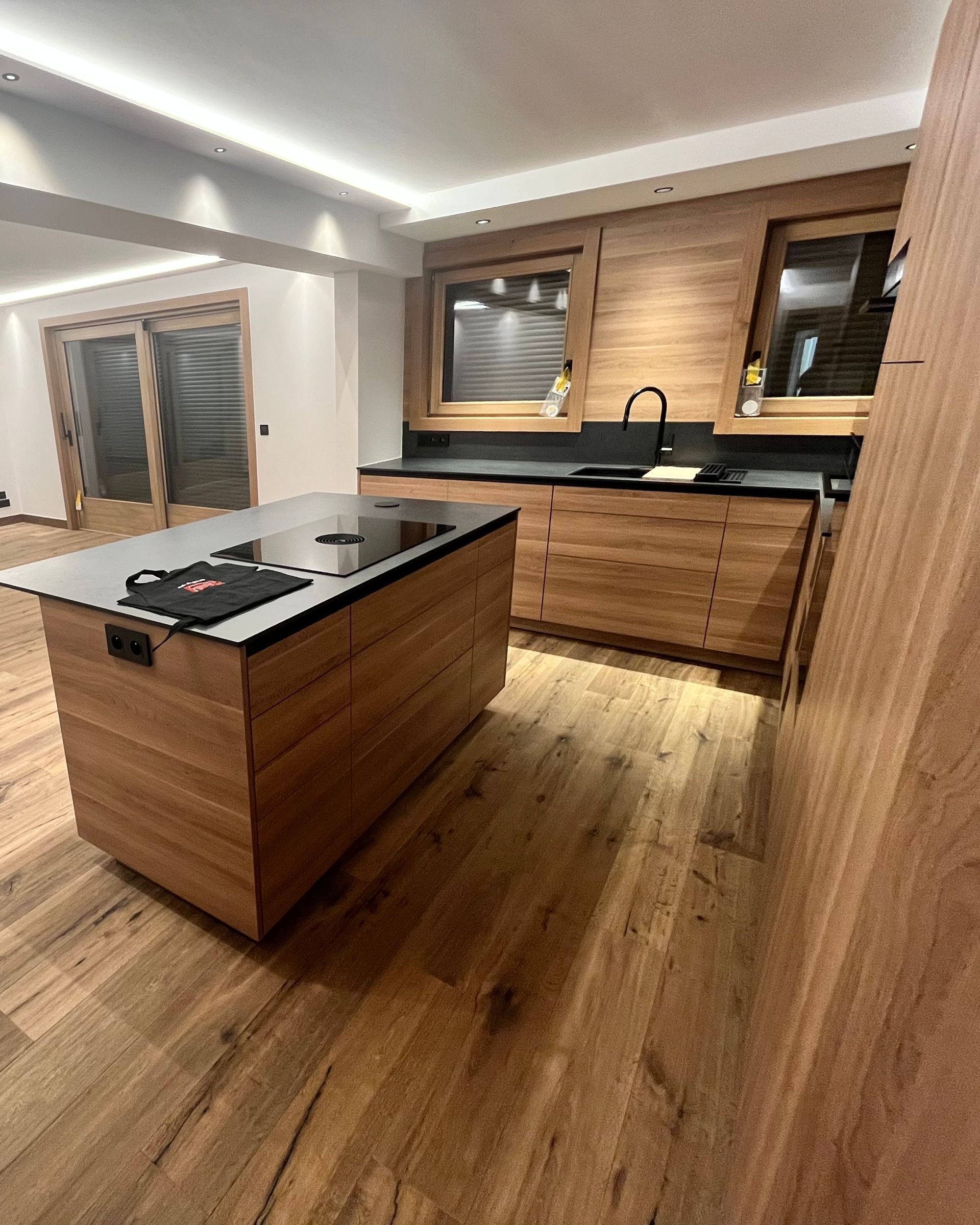 Cuisine moderne avec armoires en bois, îlot central et parquet.