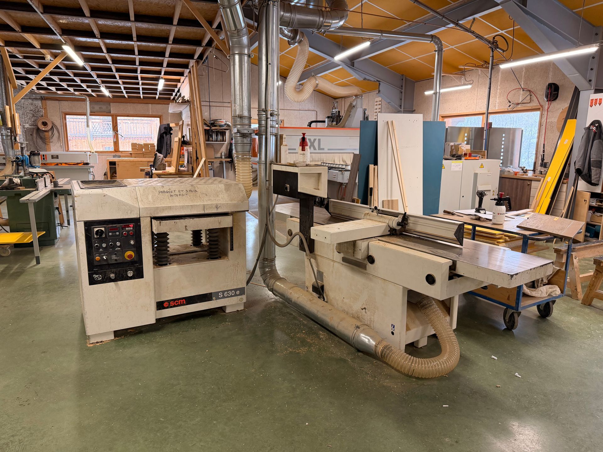 Atelier de menuiserie avec raboteuse et dégauchisseuse. Machines beiges et blanches, établi et sol en bois.