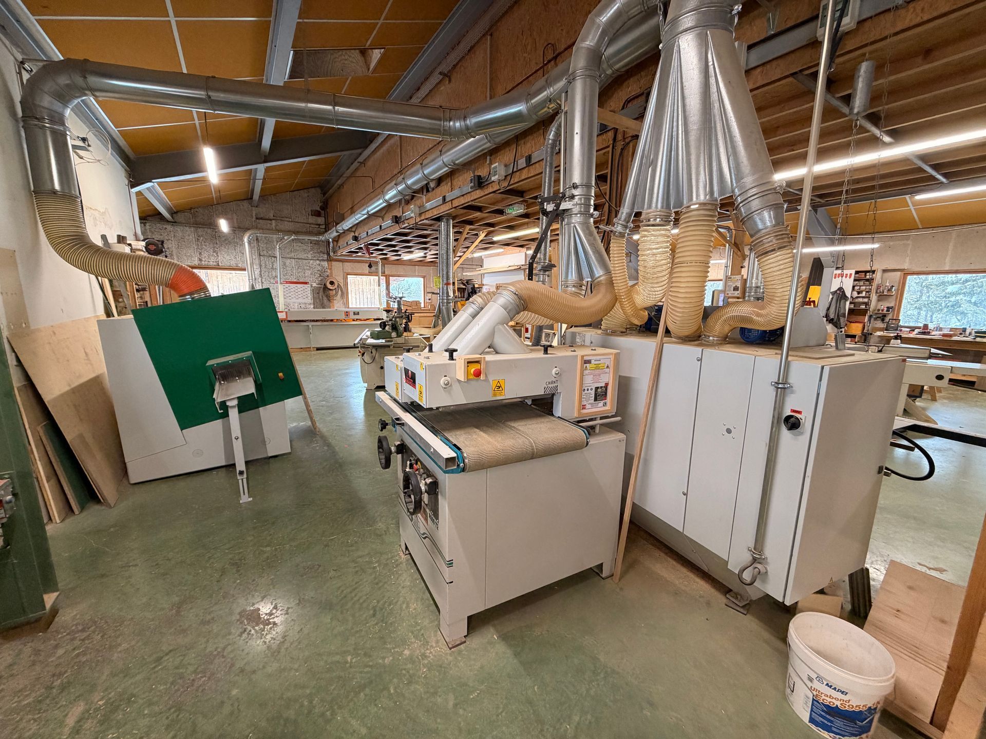 Intérieur d'un atelier avec machines à bois, conduits d'aération et un seau.