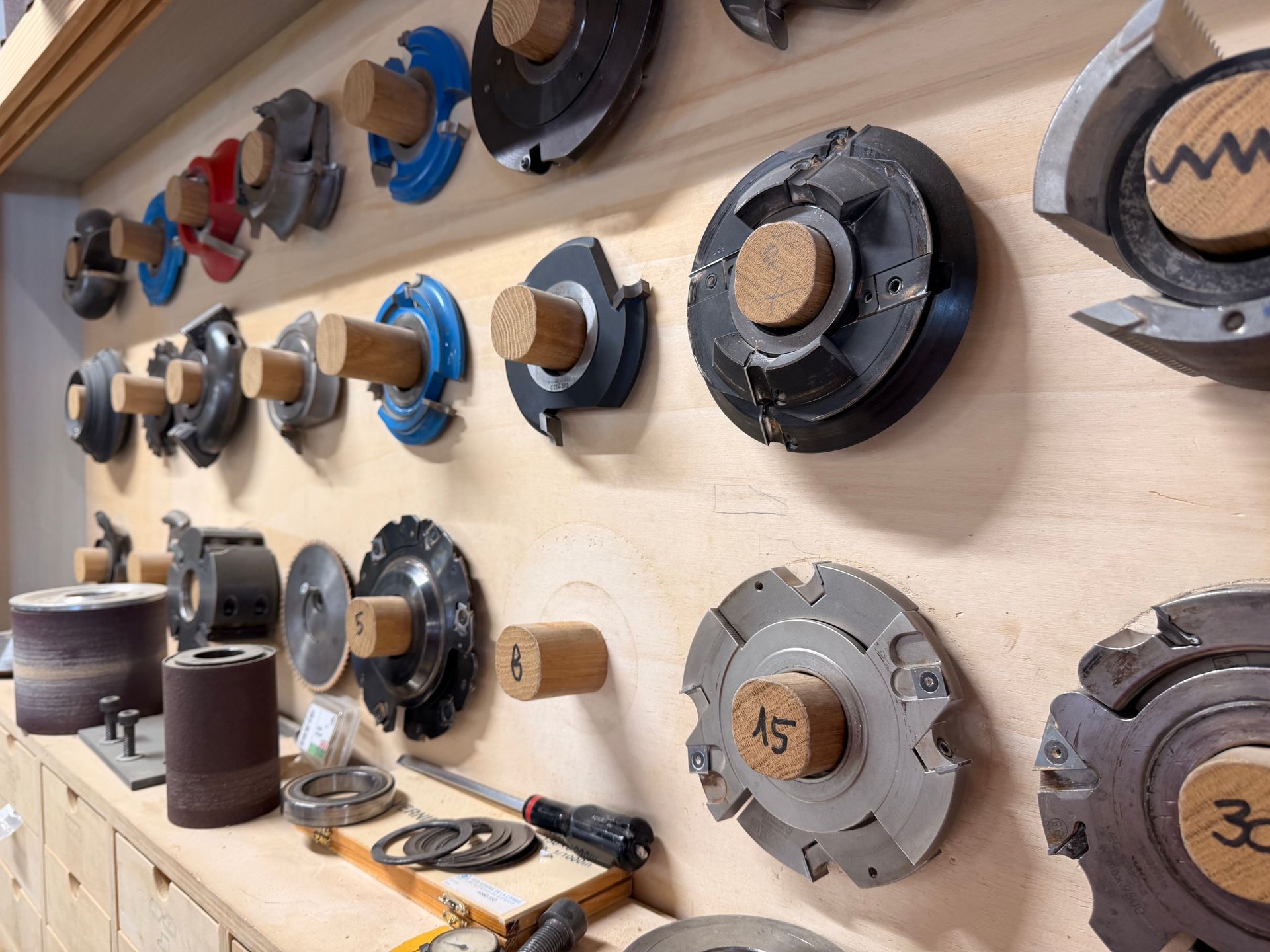 Lames de scie circulaire de différentes tailles, présentées sur un panneau perforé en bois avec supports en liège.