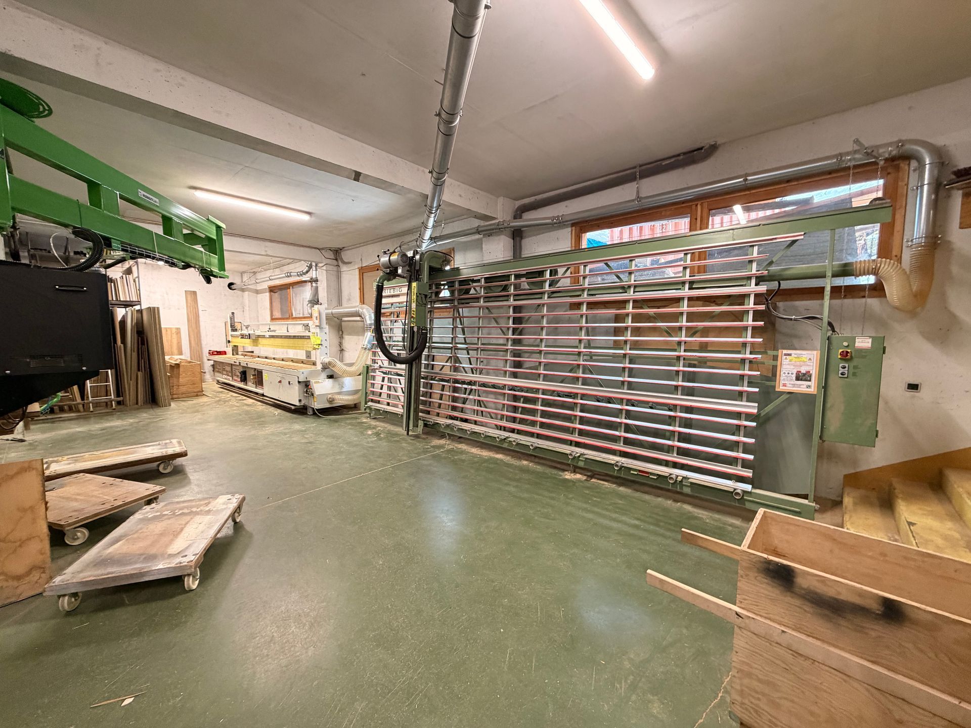 Atelier de menuiserie avec une grande scie et des machines ; sol vert, bois et éléments industriels.