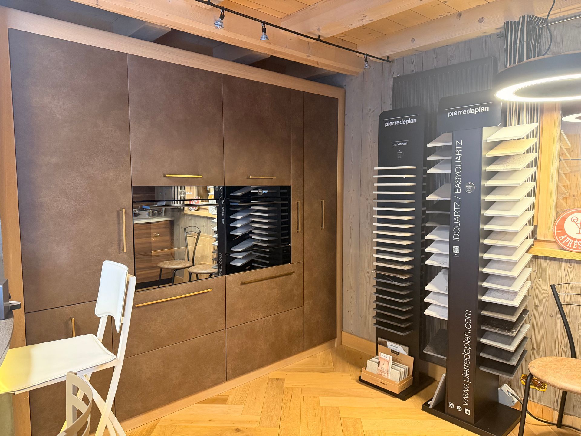 Présentation de meubles et d'échantillons dans une salle d'exposition avec four intégré et tabouret.