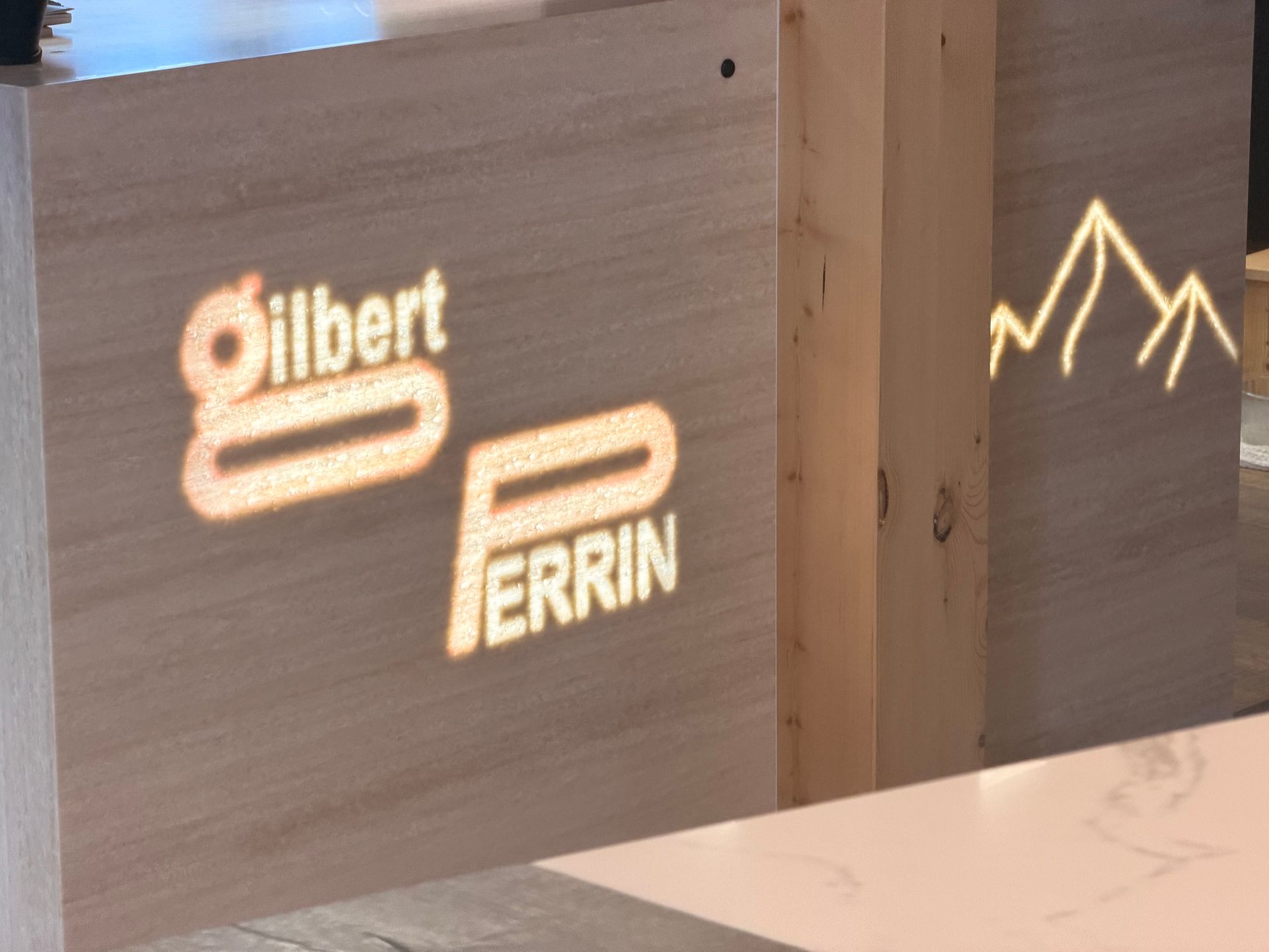 Logo « Gilbert Perrin » illuminé et silhouette de montagne projetés sur des panneaux de bois.