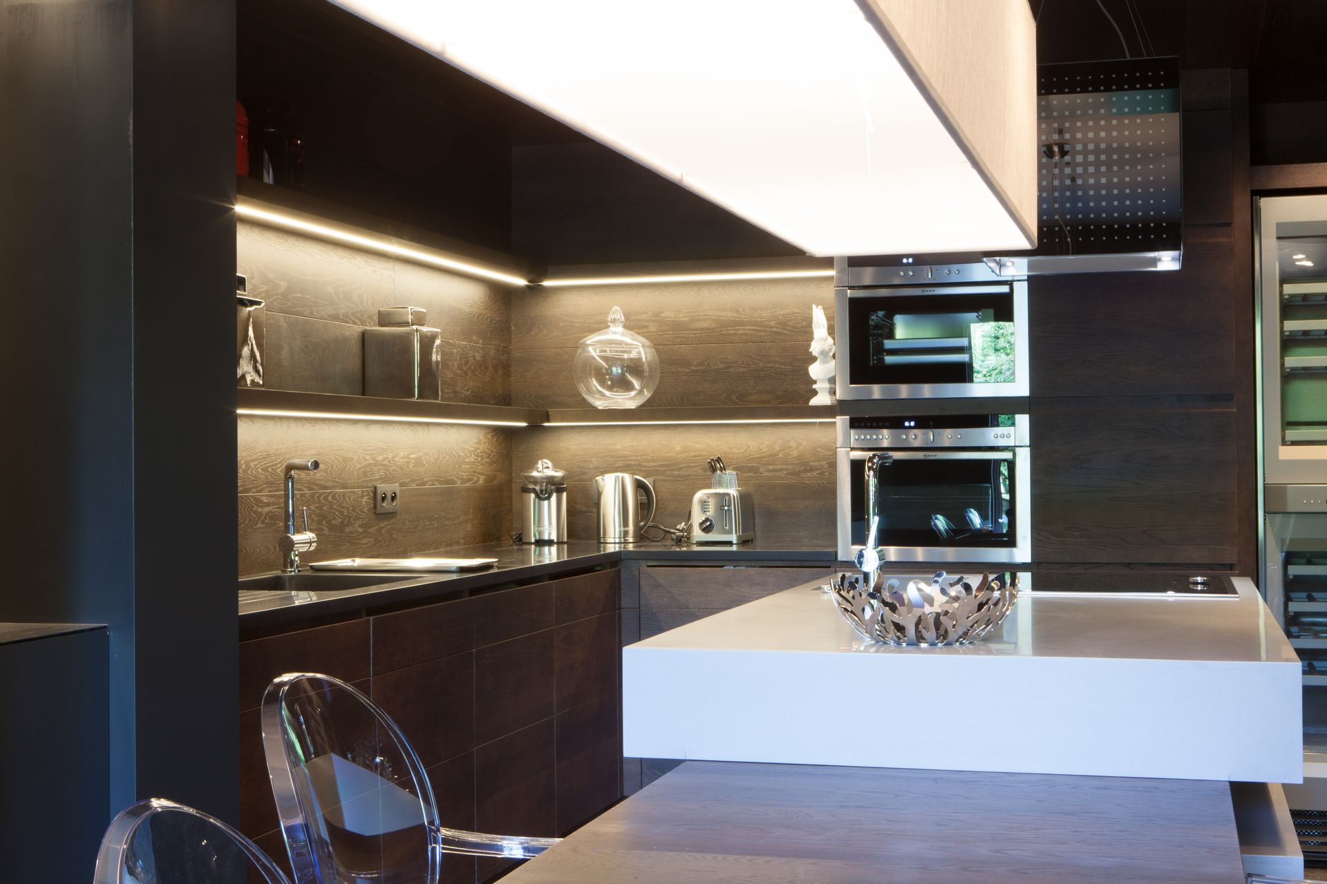 Cuisine moderne avec armoires foncées, électroménagers en acier inoxydable et îlot blanc.