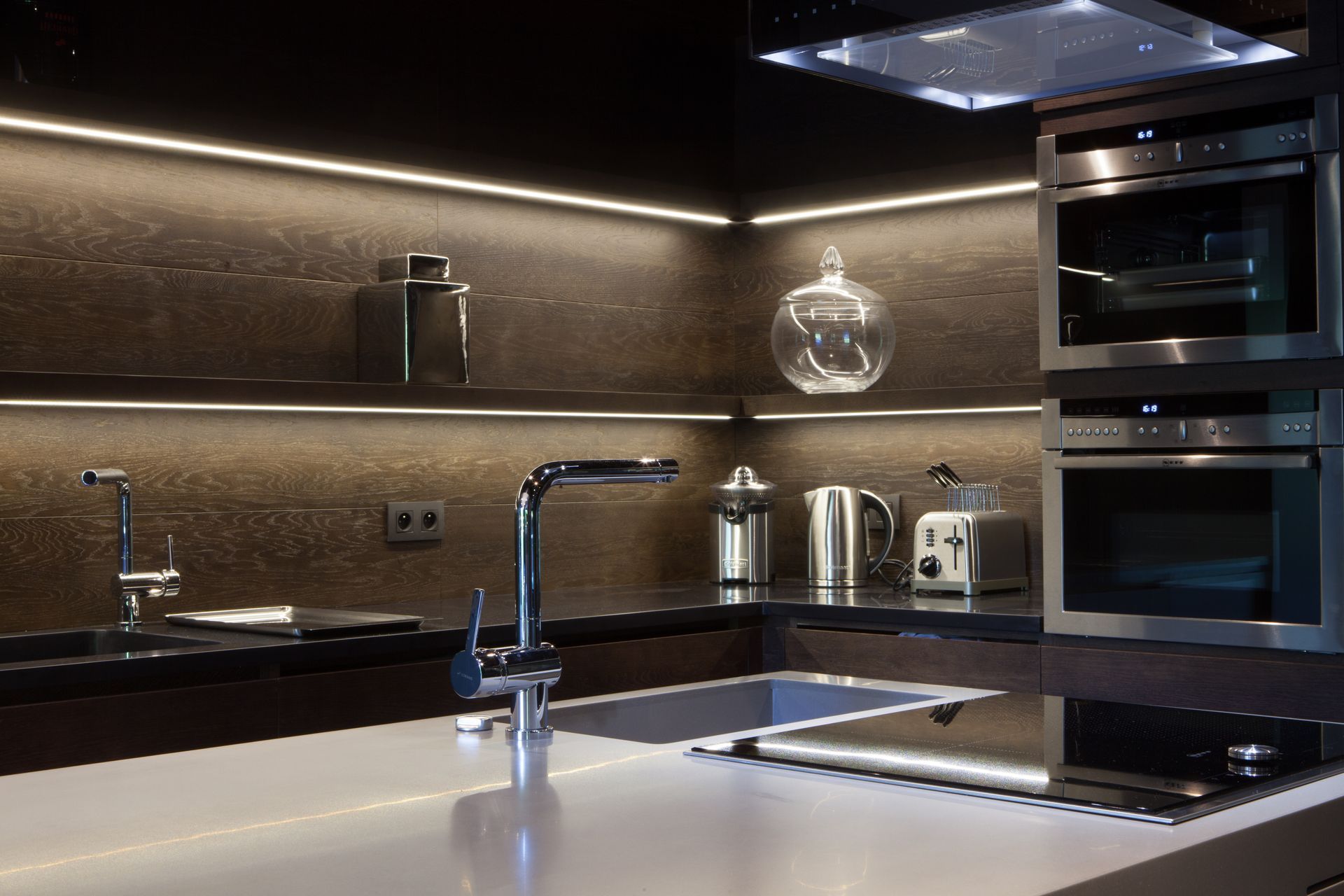 Cuisine moderne avec appareils électroménagers en acier inoxydable, armoires foncées et comptoir clair avec plaque de cuisson intégrée.