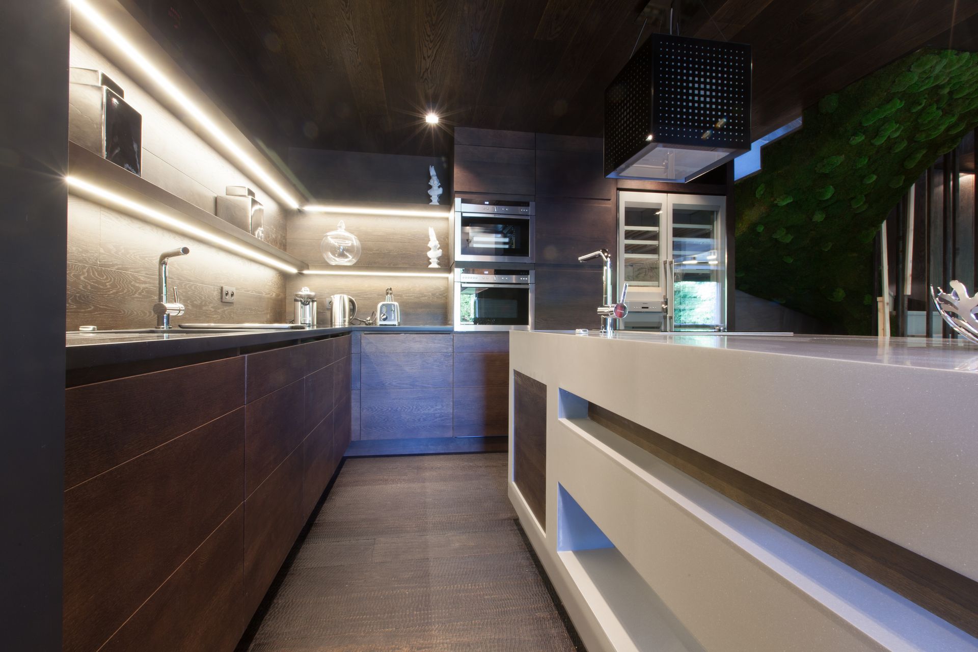 Cuisine moderne avec armoires en bois, appareils électroménagers en acier inoxydable et îlot central avec comptoir blanc.