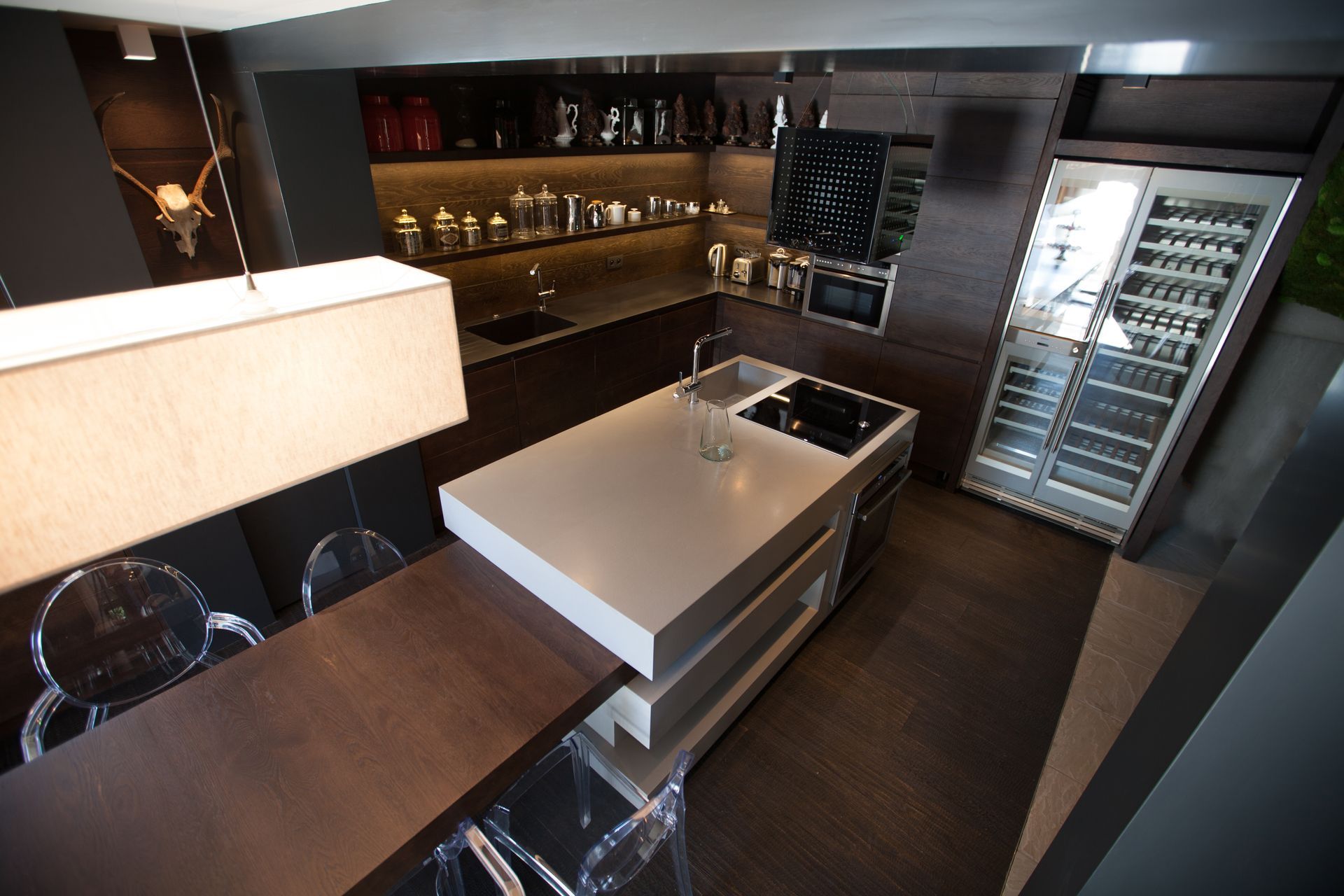 Cuisine moderne avec plan de travail blanc, placards foncés et porte ouverte sur un espace vert.