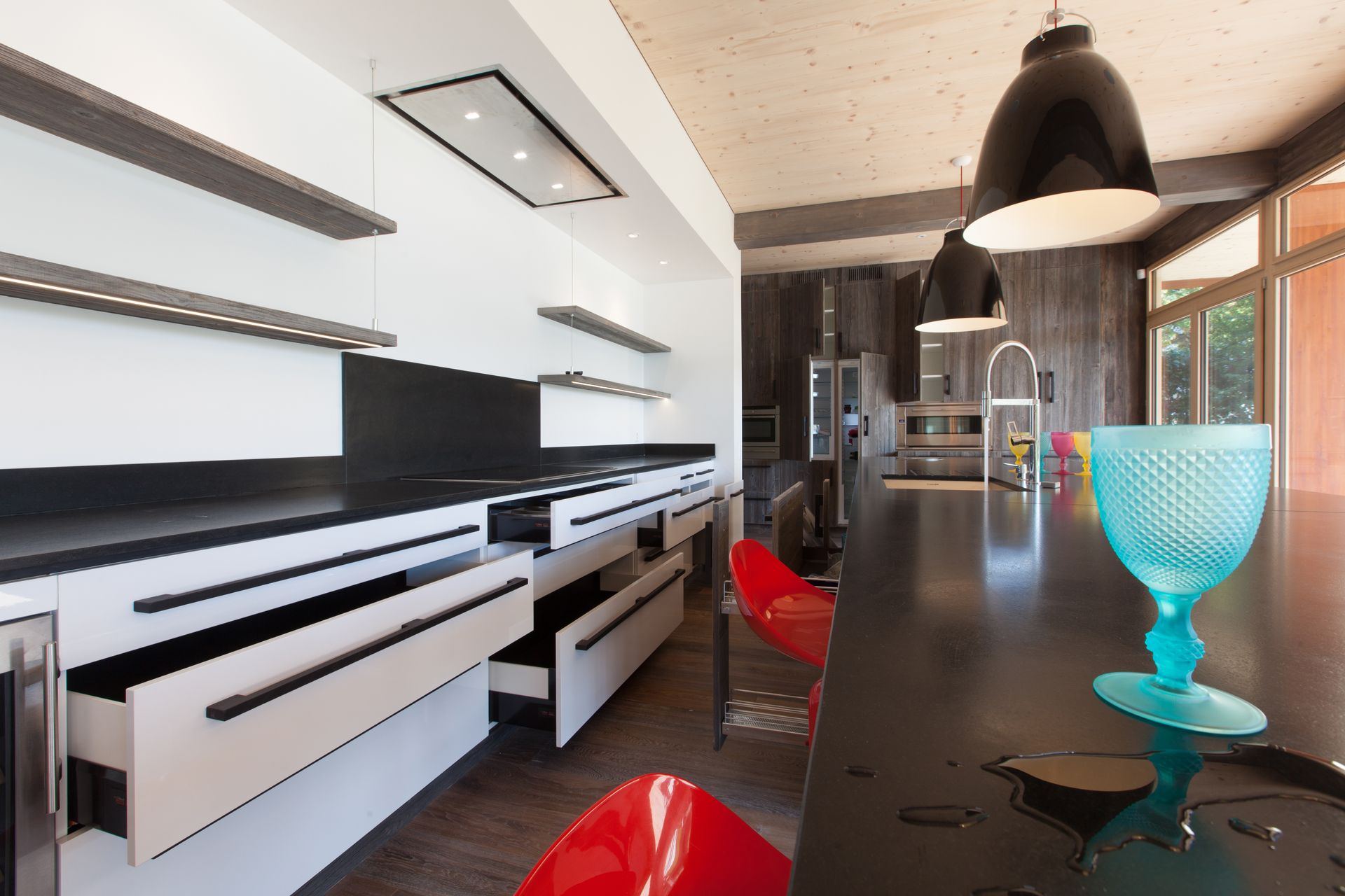 Cuisine moderne avec comptoirs noirs, armoires blanches et tabourets de bar rouges. Un verre bleu est posé sur le comptoir.