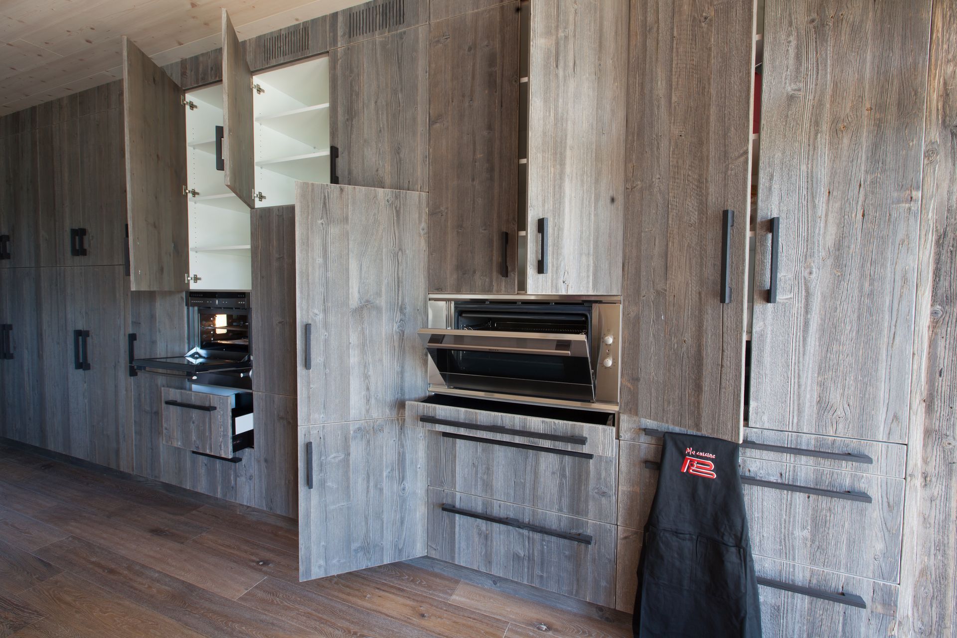 Cuisine équipée en bois avec électroménager, certaines portes ouvertes.