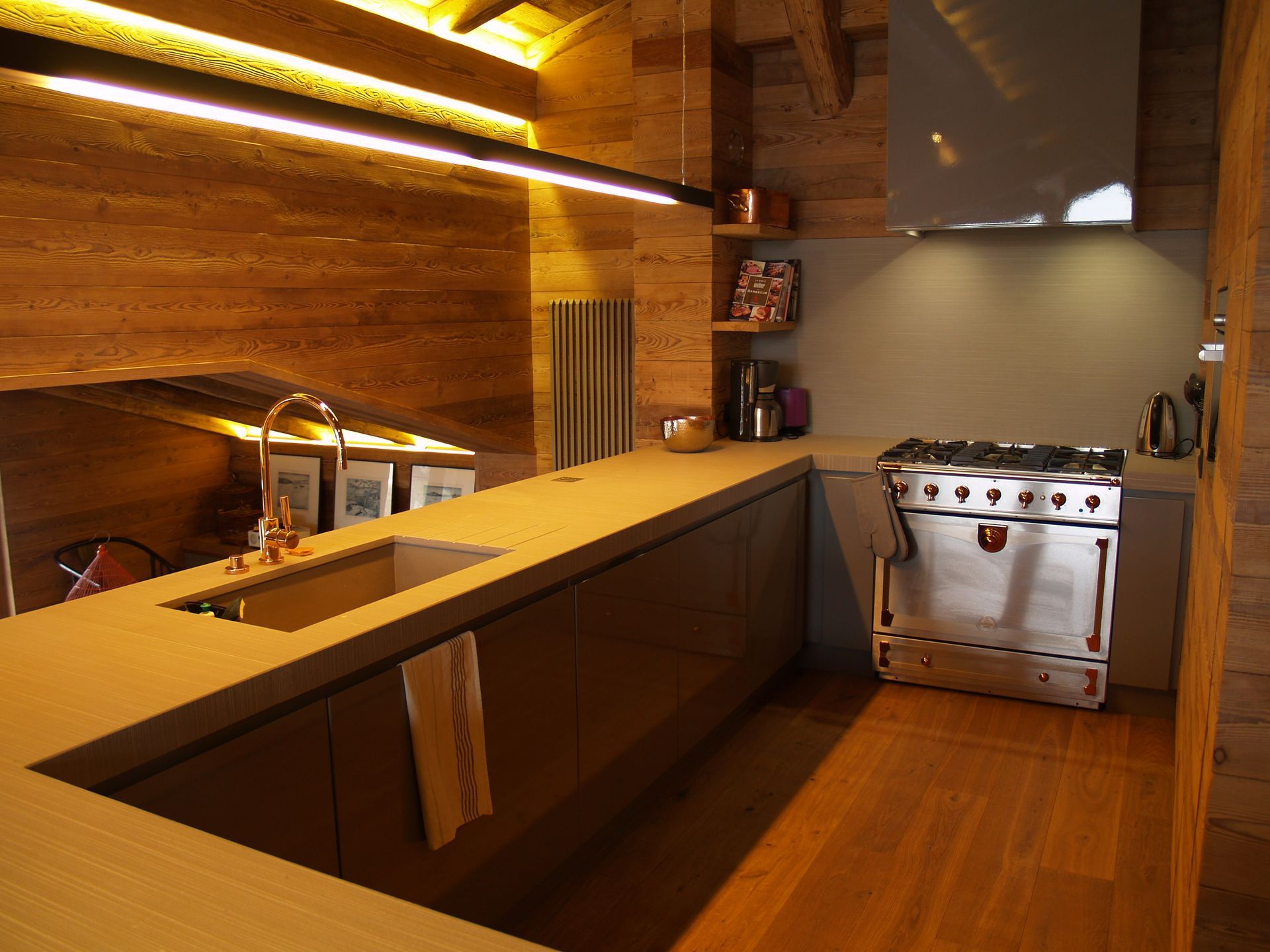 Cuisine moderne avec murs et placards en bois, cuisinière en acier inoxydable et plan de travail clair.