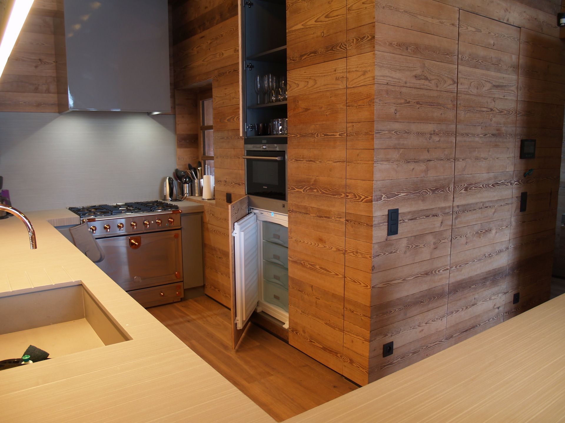 Cuisine avec murs et placards lambrissés, appareils électroménagers en acier inoxydable et plan de travail clair.