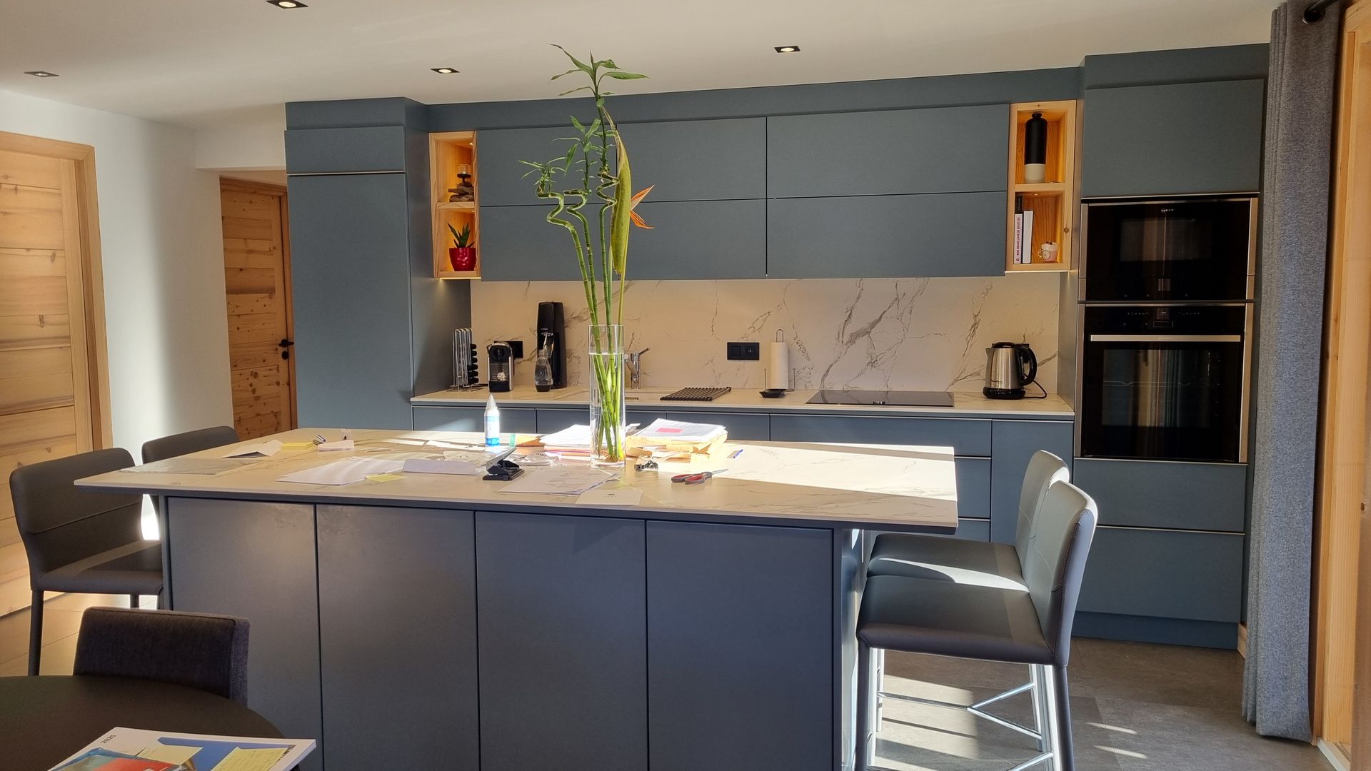 Cuisine moderne avec placards bleus, îlot central avec sièges, fours encastrés et plan de travail clair.