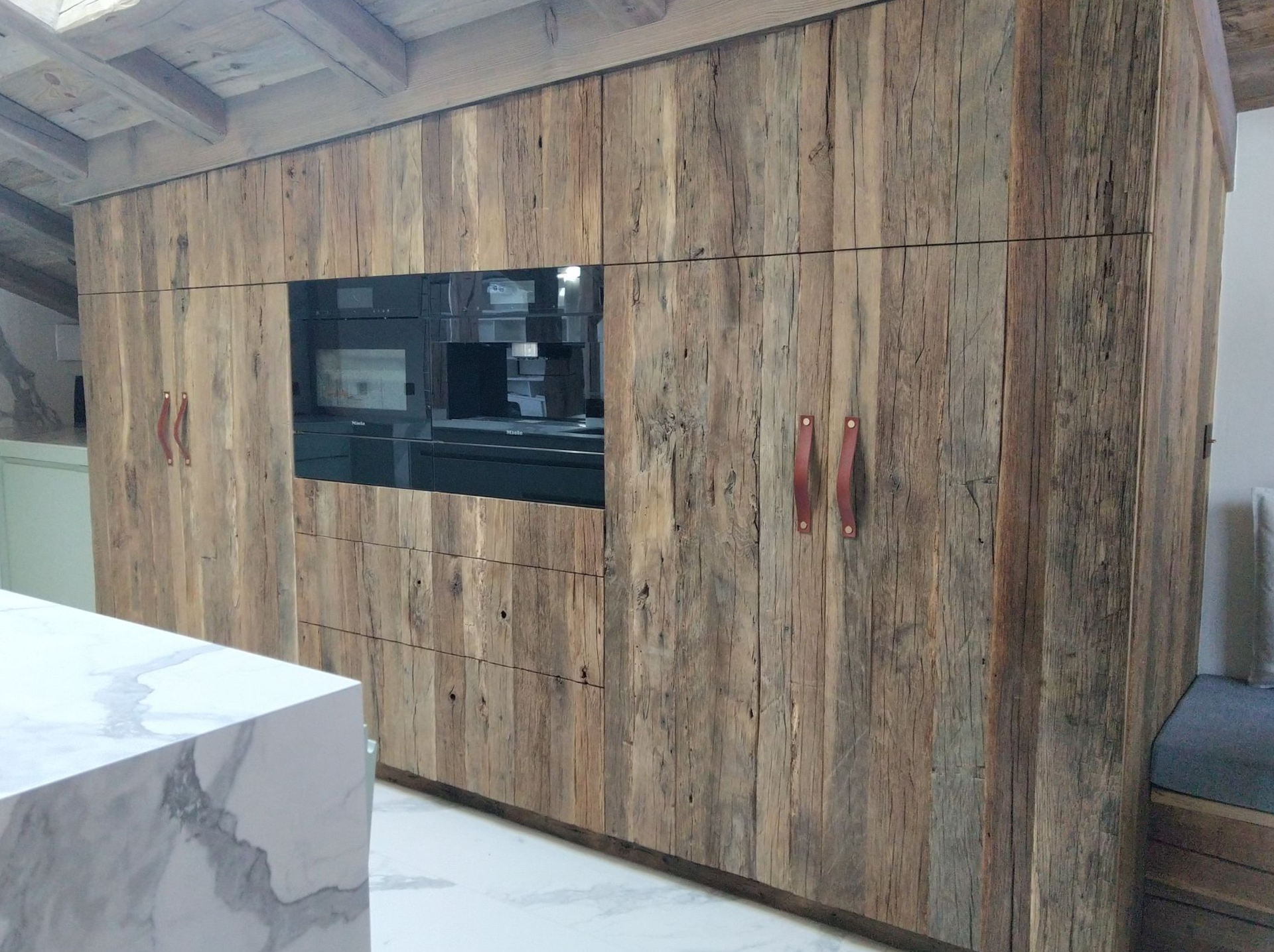 Meubles de cuisine en bois avec four et micro-ondes intégrés. Plan de travail en marbre clair au premier plan.